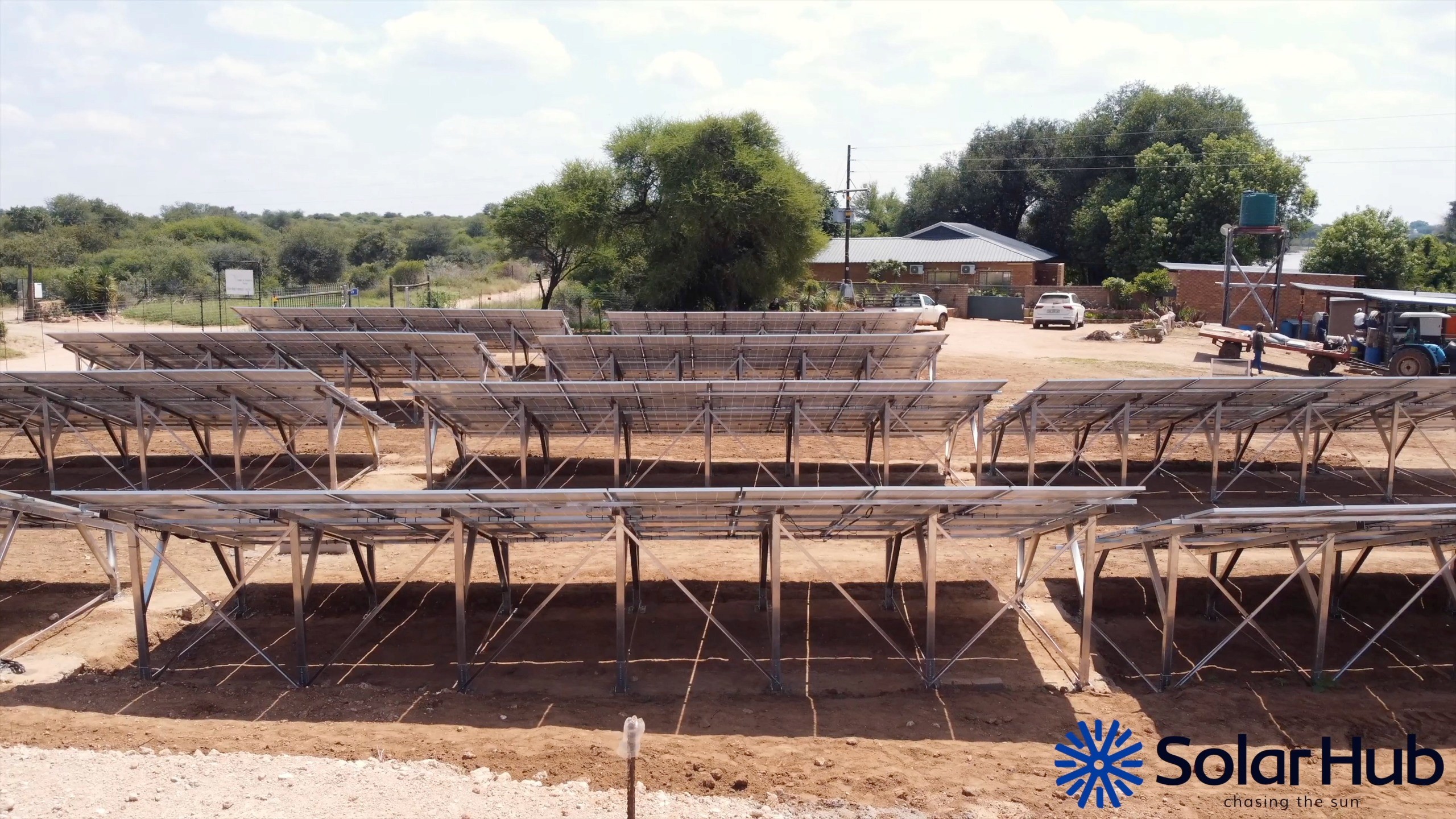 Woman in a beige blazer handing a document to someone, standing near a window with a city view. She looks professional and confident.