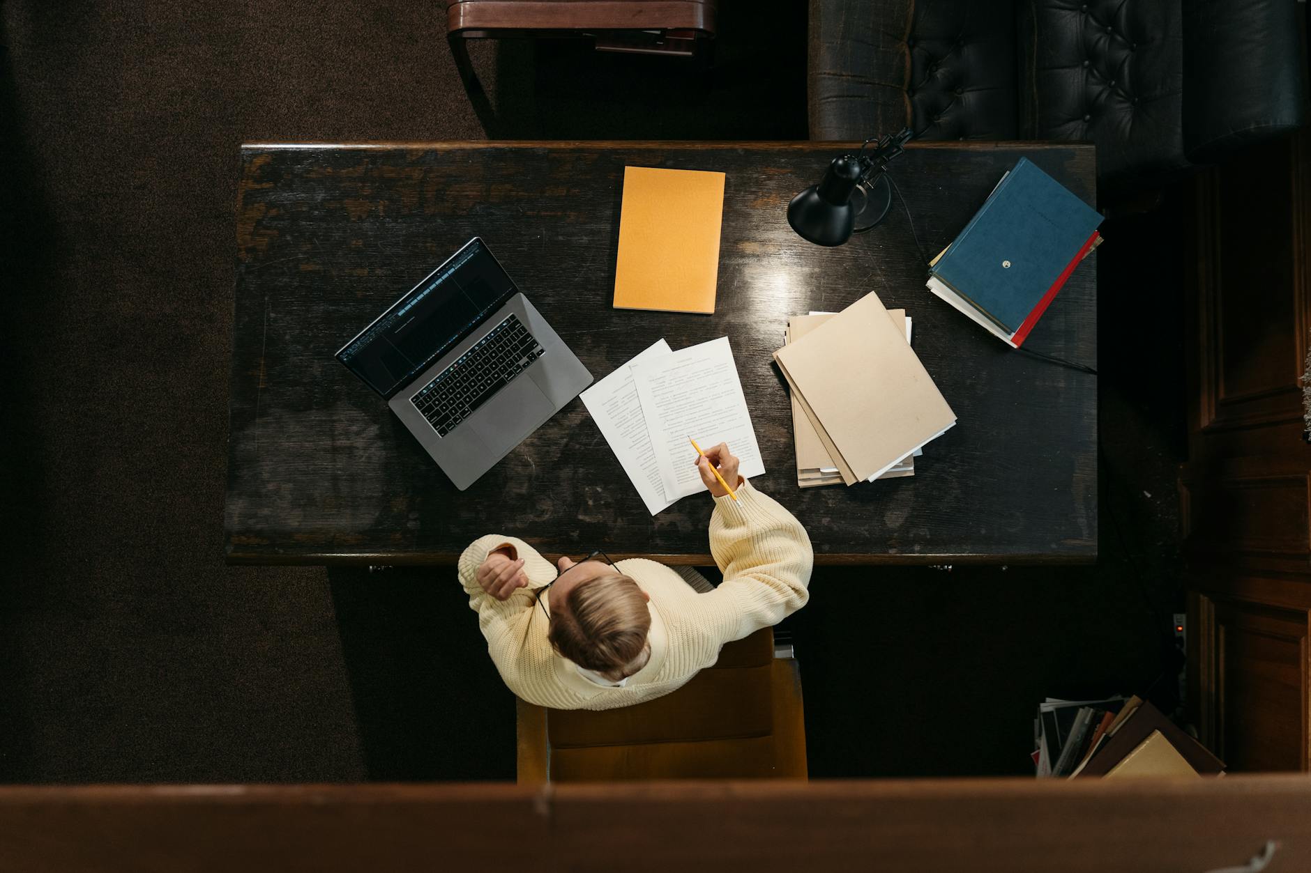 A focused student reviews a checklist and application documents on a laptop at a wooden desk.