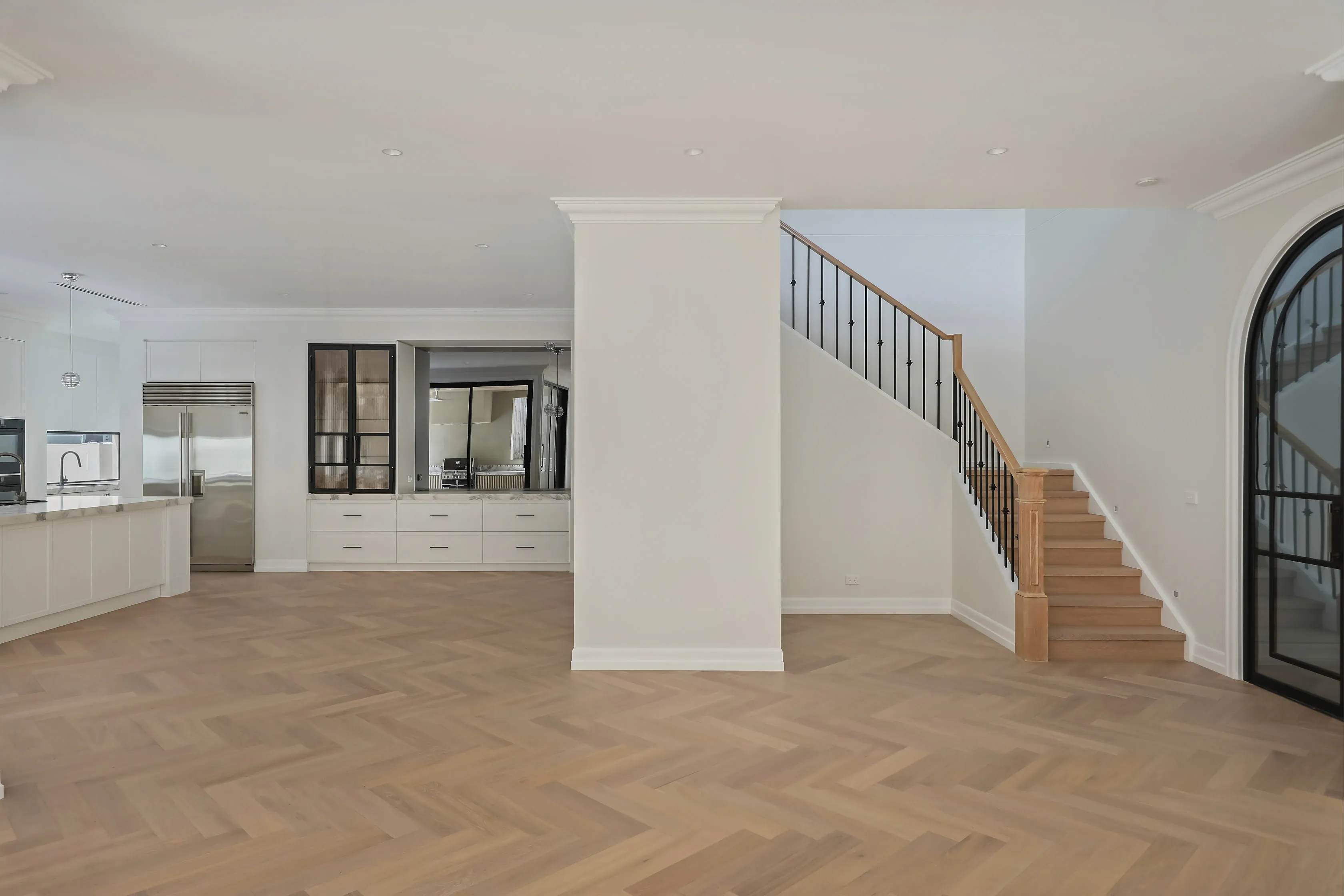 Templestowe living space with a timber-and-wrought-iron staircase, arched black steel-framed door and herringbone oak floor