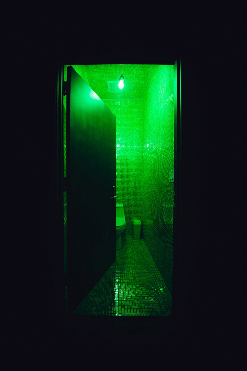 The "green tile" bathroom in the washroom at Particle Studio in Seattle, WA. It features a green toilett, green tile walls and a bright green light bulb splasing neon green light everywhere.