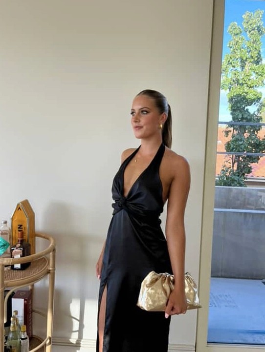 Black satin halter dress with deep V neckline, twisted bust detail, fluid drape, and thigh-high front slit