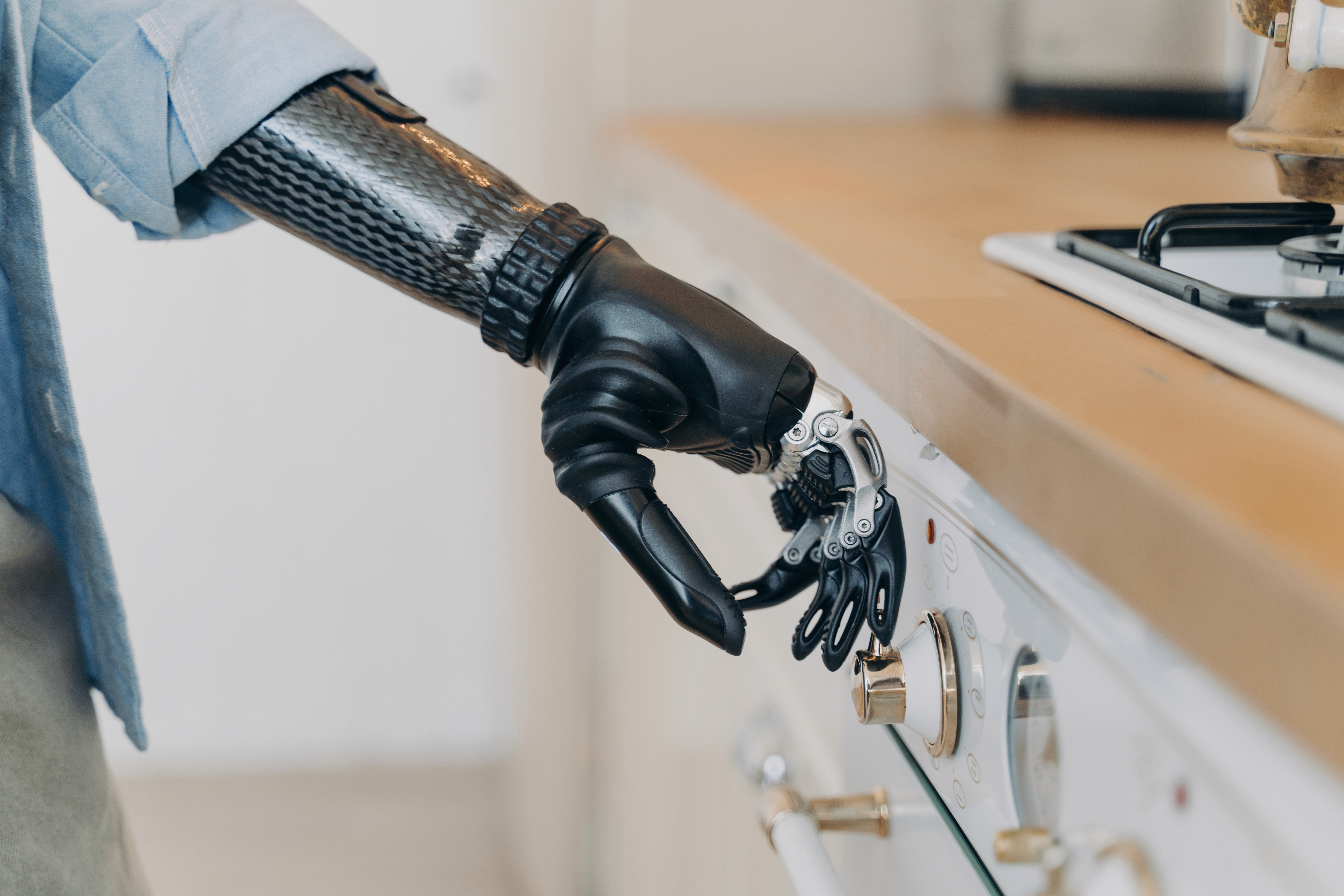Person using advanced prosthetic arm to operate gas stove knob in kitchen setting