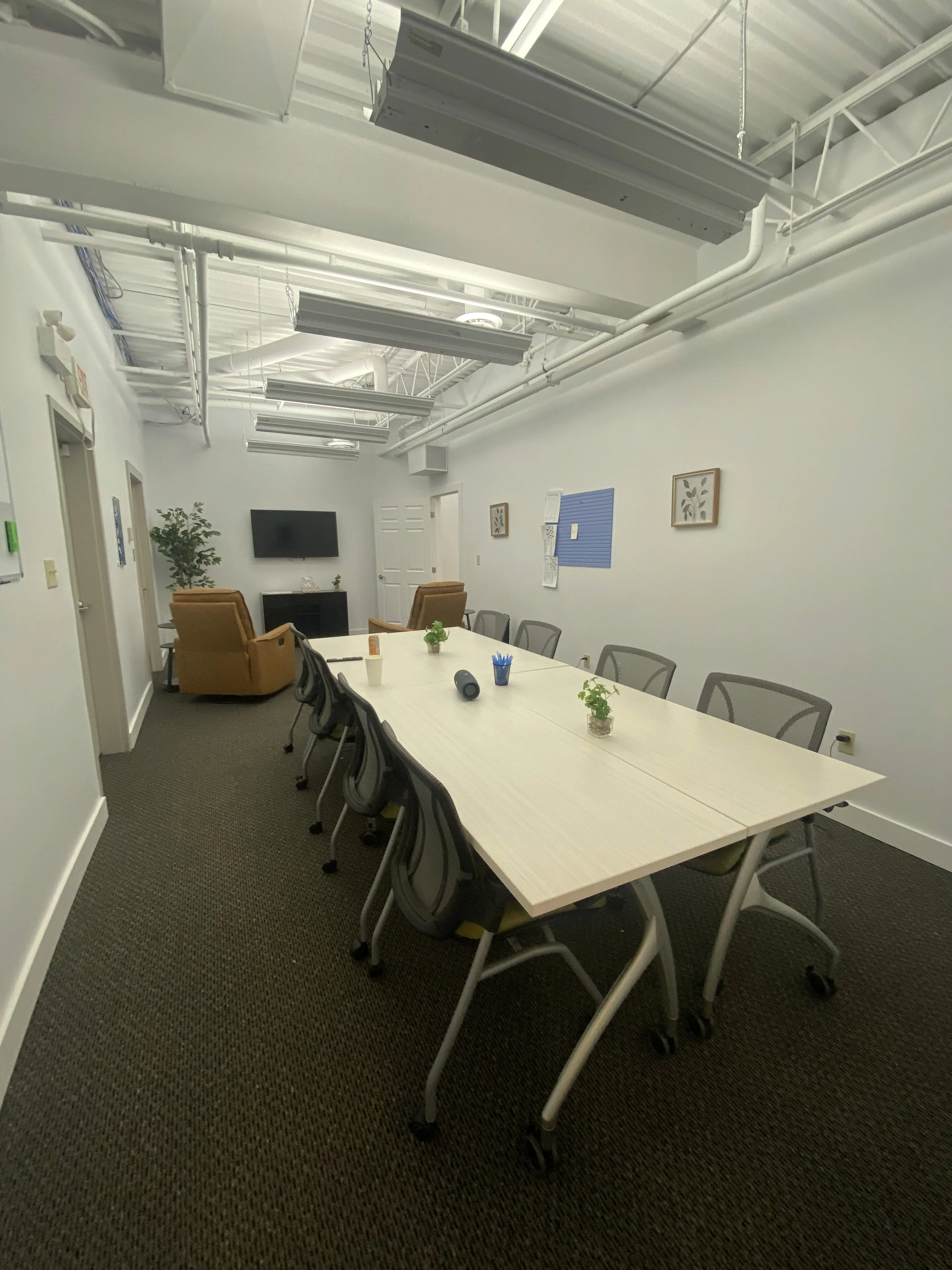 Meeting room with a long conference table, rolling chairs, a wall-mounted TV, and tan recliner chairs