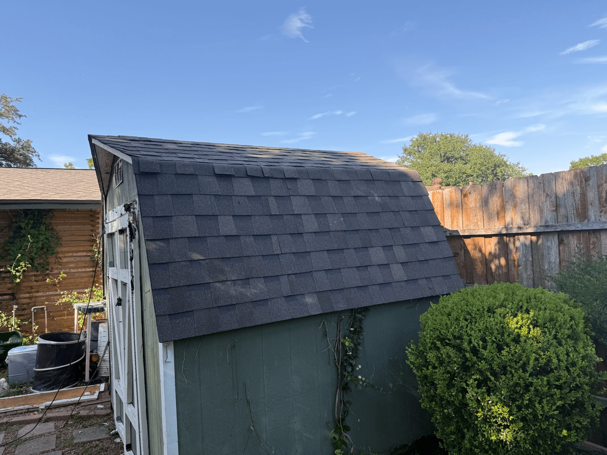 residential roofing services in Arlington installing new asphalt shingles on a backyard storage shed.