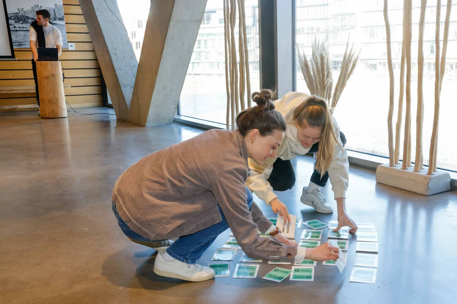 Zwei junge Frauen spielen ein Kartenspiel auf dem Boden eines Meetingraums