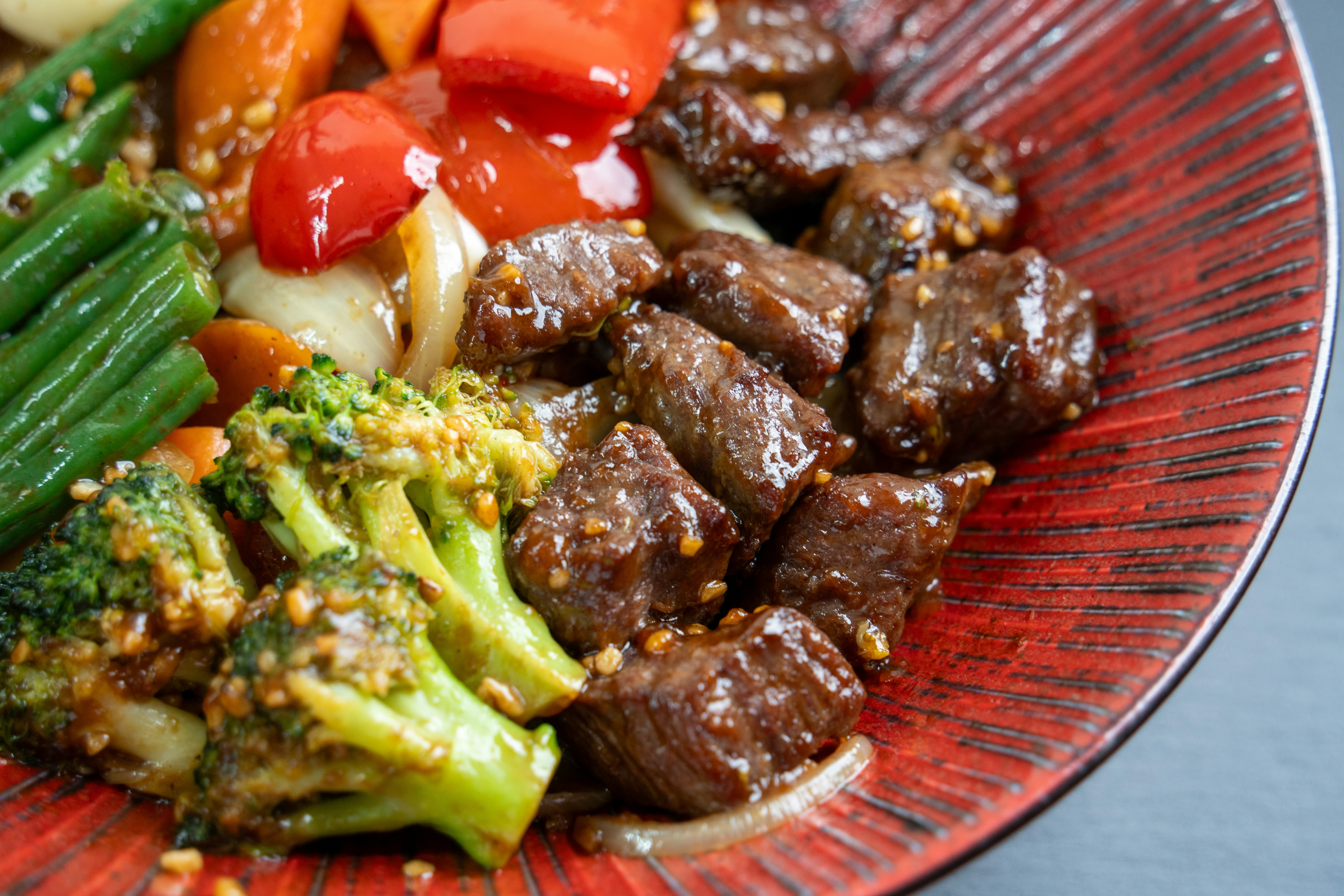 Beef and broccoli stir-fry with vegetables on a red plate
