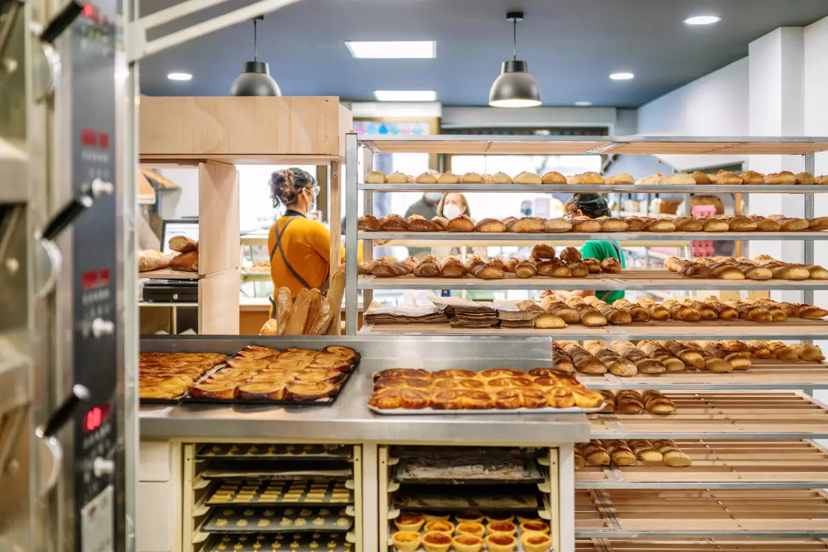 Back of a bakery with sales clerks selling bread to customers and carts with loaves and cakes fresh