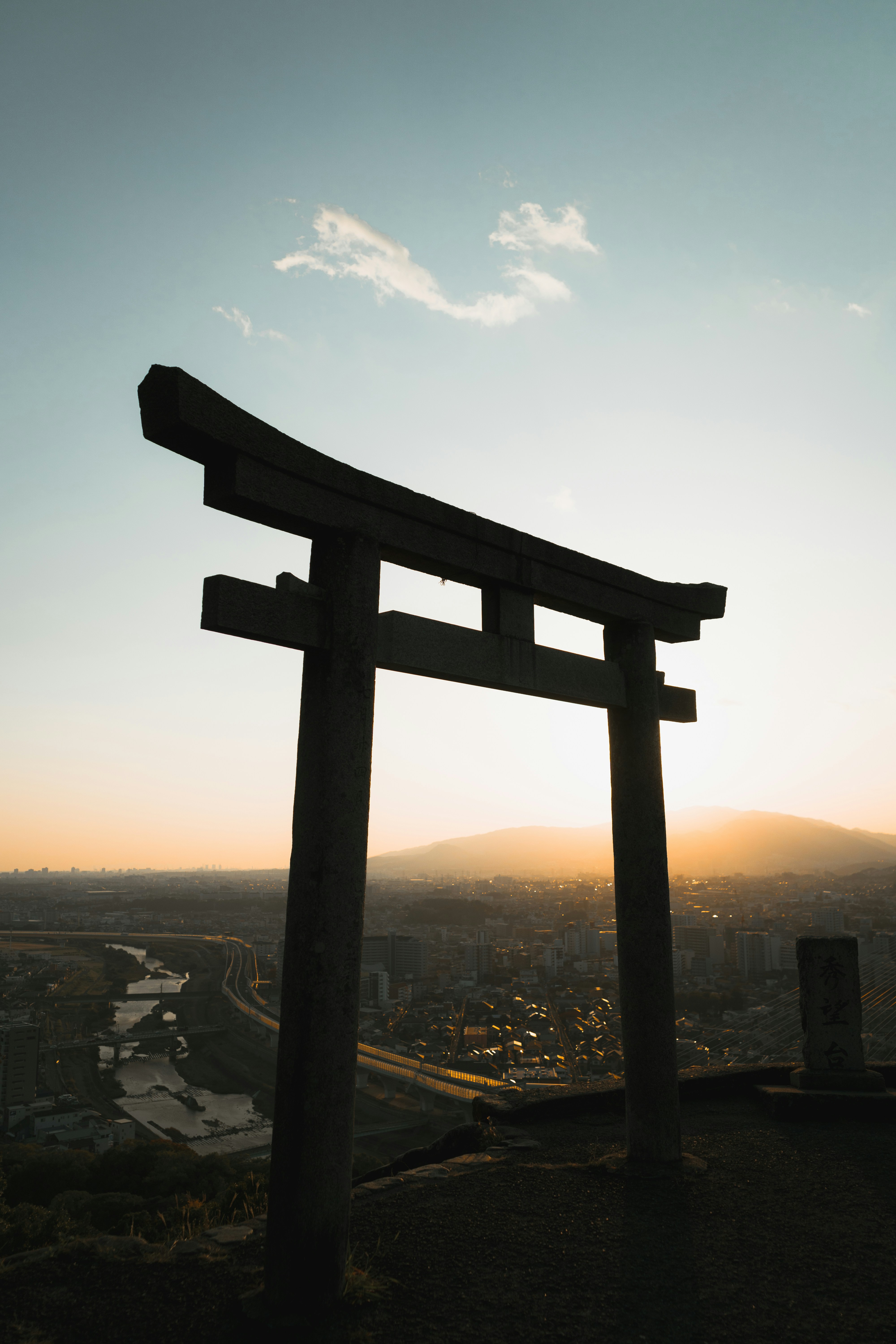 Torii gate silhouetted against a sunset over a city.