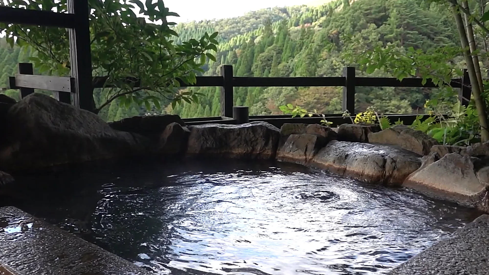 A dark open-air pool behind a timber rail at Kurokawa Onsen, forest beyond