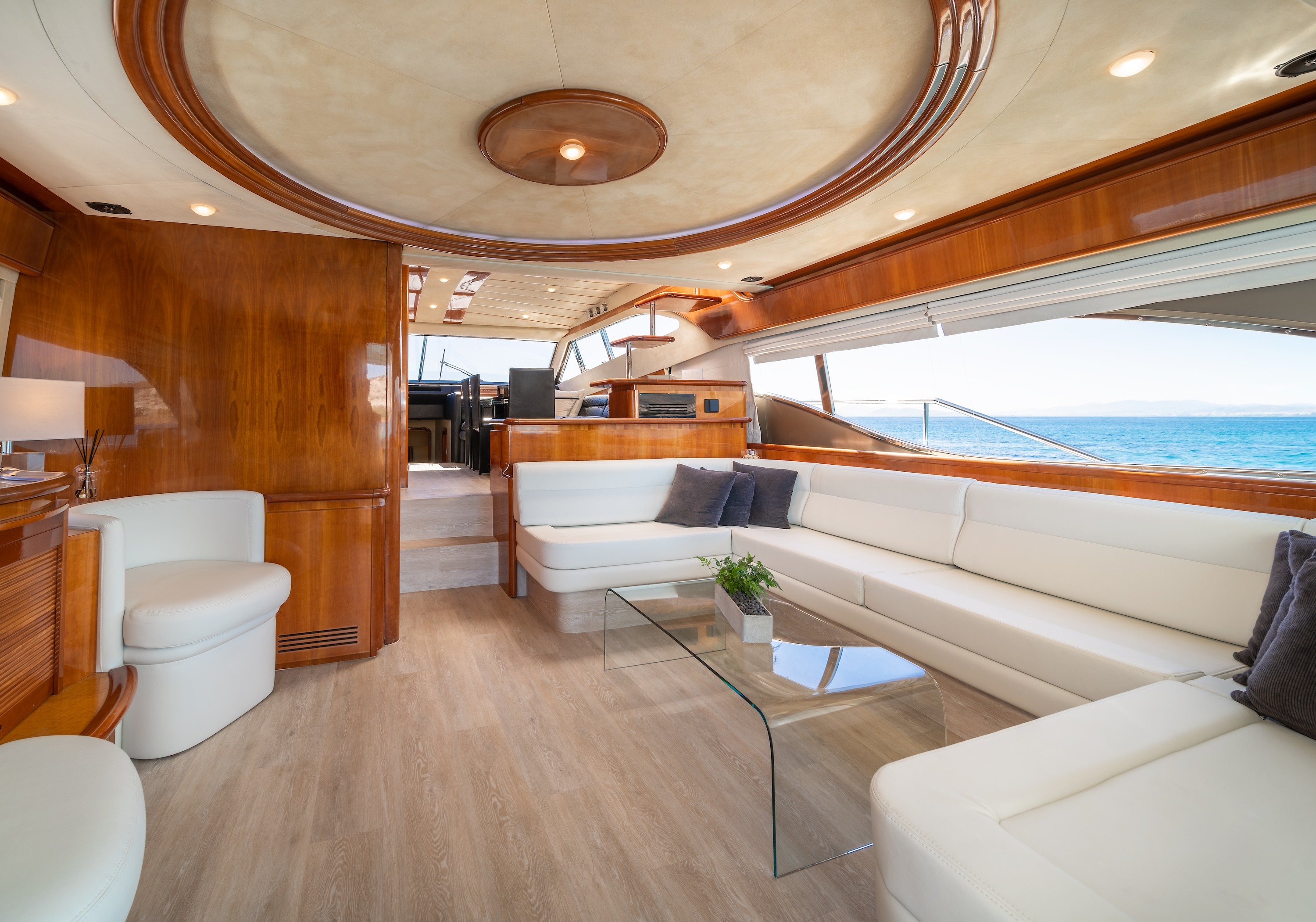 Luxurious main salon interior of Ferretti 68 yacht with white leather seating, wood finishes, and panoramic windows overlooking turquoise waters.