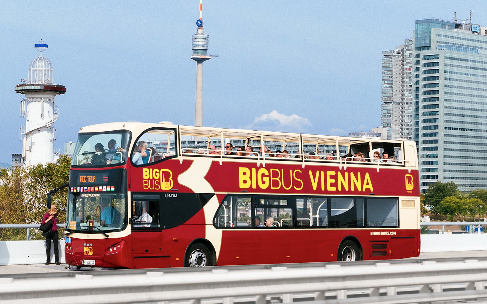 Touristen auf dem Big Bus Wien mit Riesenrad und Donaukreuzfahrt im Hintergrund.