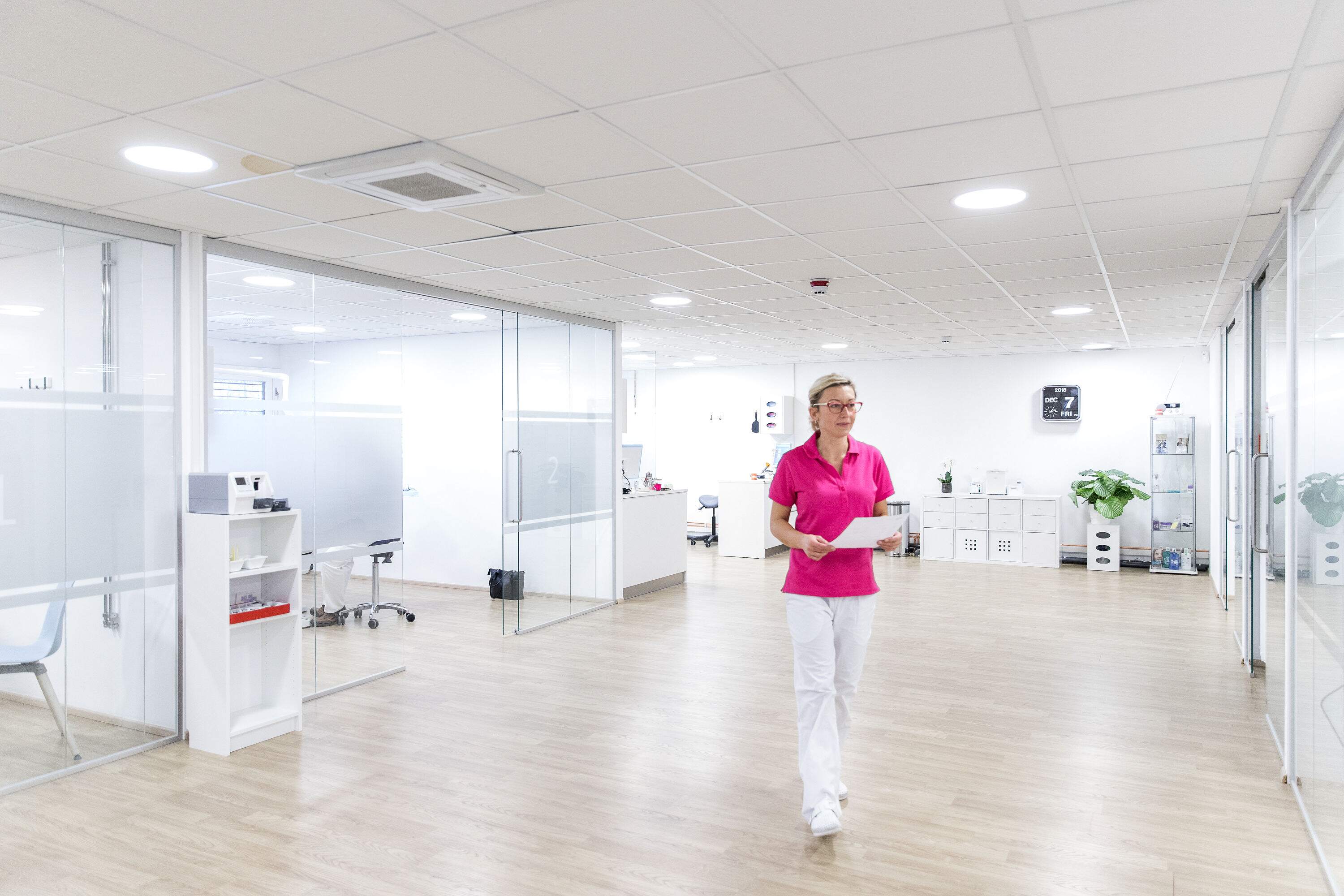 Tannlege ved Haugenstua Tannlegesenter går gjennom den lyse og moderne klinikken i Oslo, med glassvegger og hyggelig atmosfære.”