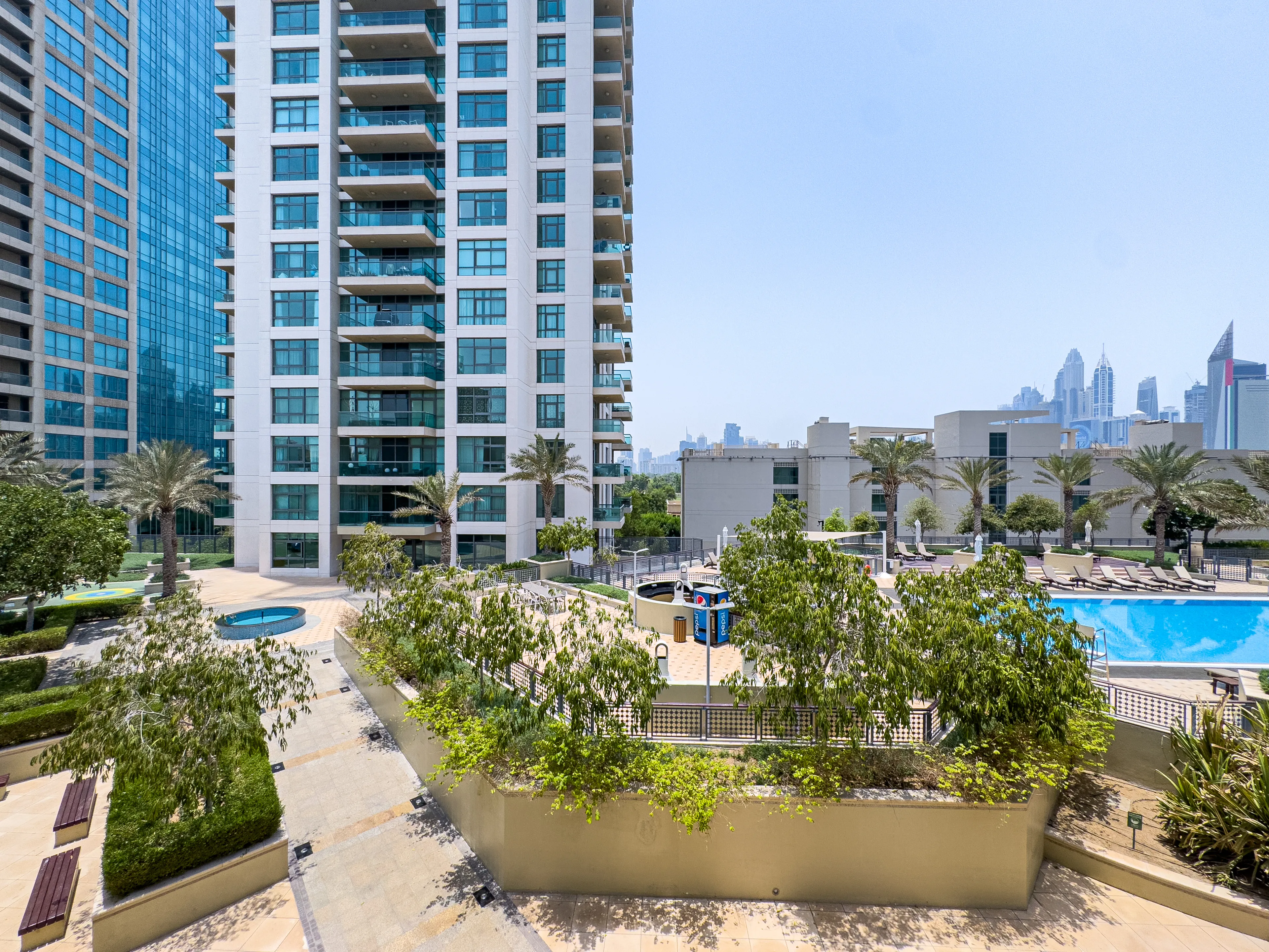 Image of a Dubai pool place with trees and skyscrapers.