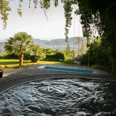 Sprudelnder Whirlpool im Garten, dahinter Palme, Pool und der Blick ins Tal