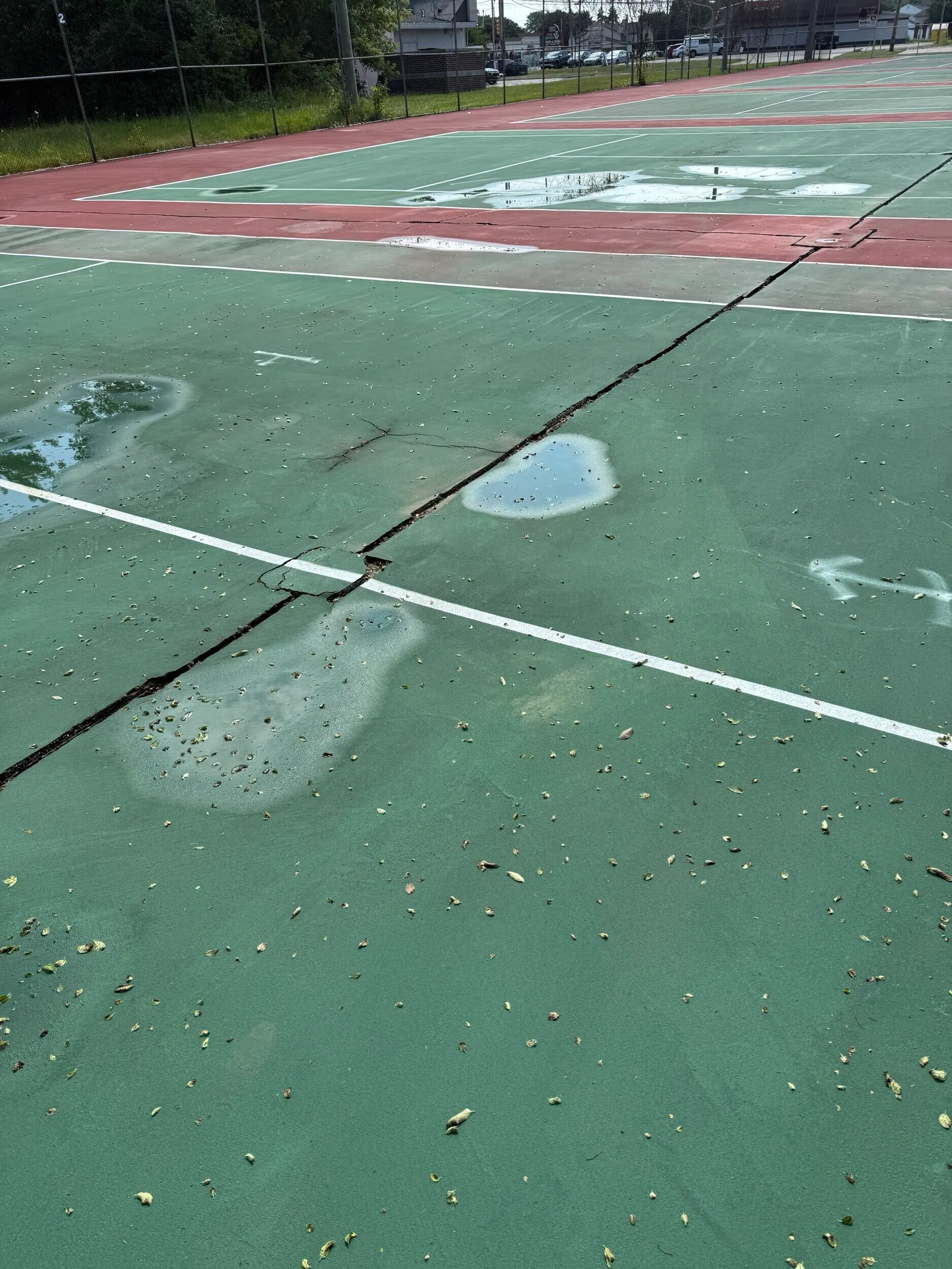 Long surface crack and standing water on tennis courts before conversion to pickleball courts