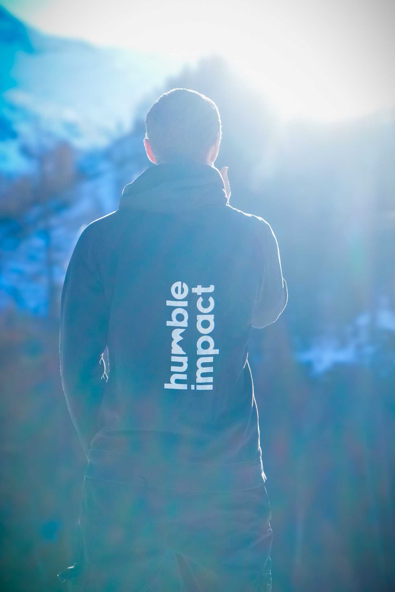 Three people in conversation with warm lighting, including a person wearing a hat and another person wrapped in what appears to be a textured shawl or sweater.
