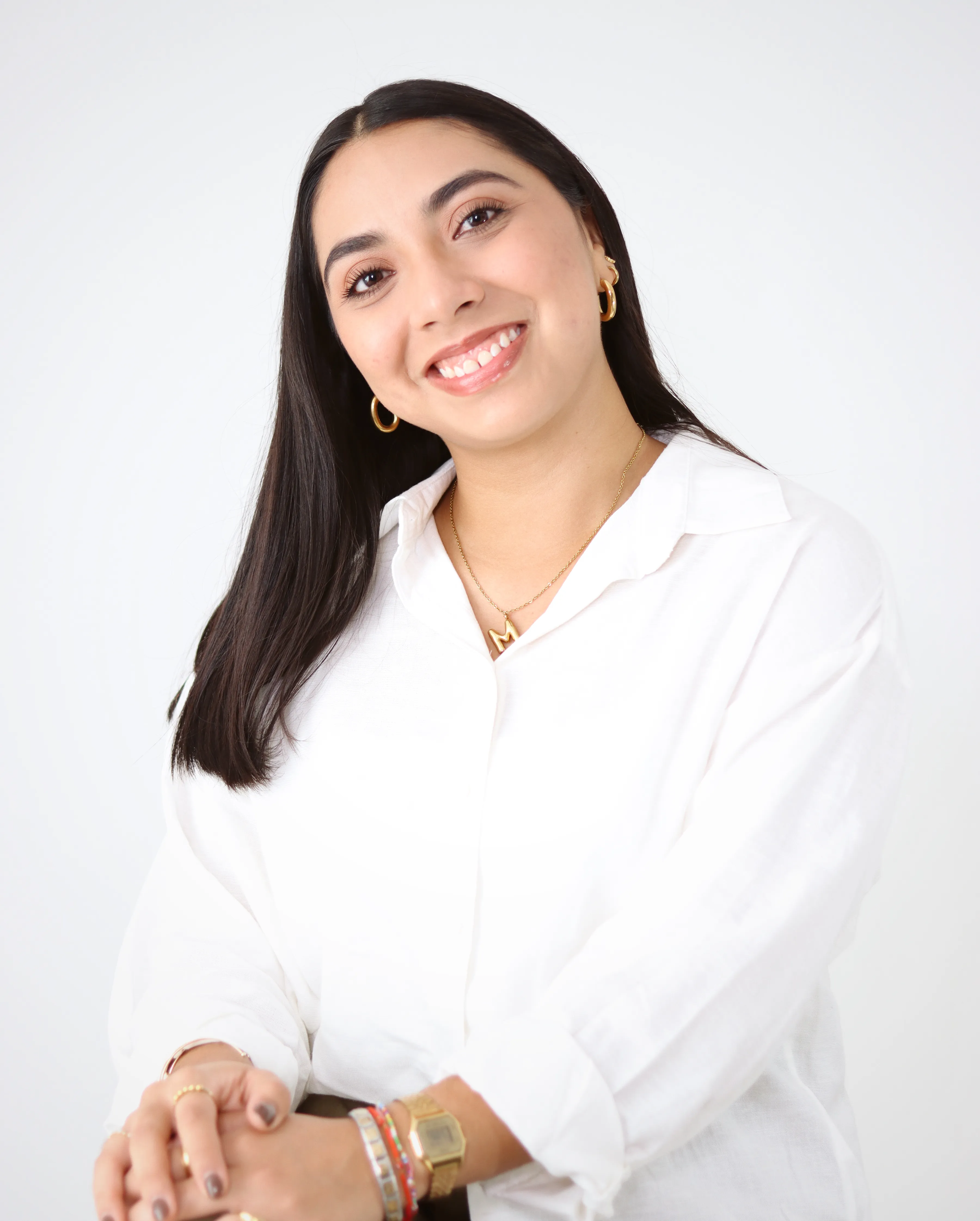 Retrato de mujer sonriendo con camisa blanca sobre fondo claro.