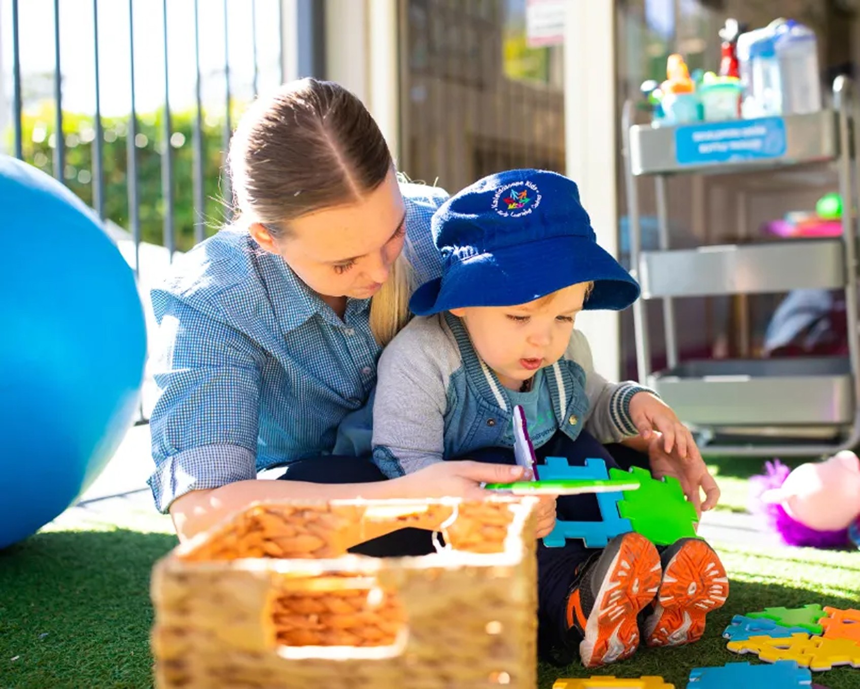 Young child playing on an outdoor tricycle while holding a soft toy at Kaleidoscope Kids childcare centre in Brisbane.