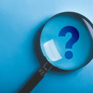 A large magnifying glass rests on a bright blue surface, focusing on a prominent question mark, symbolizing inquiry and exploration.