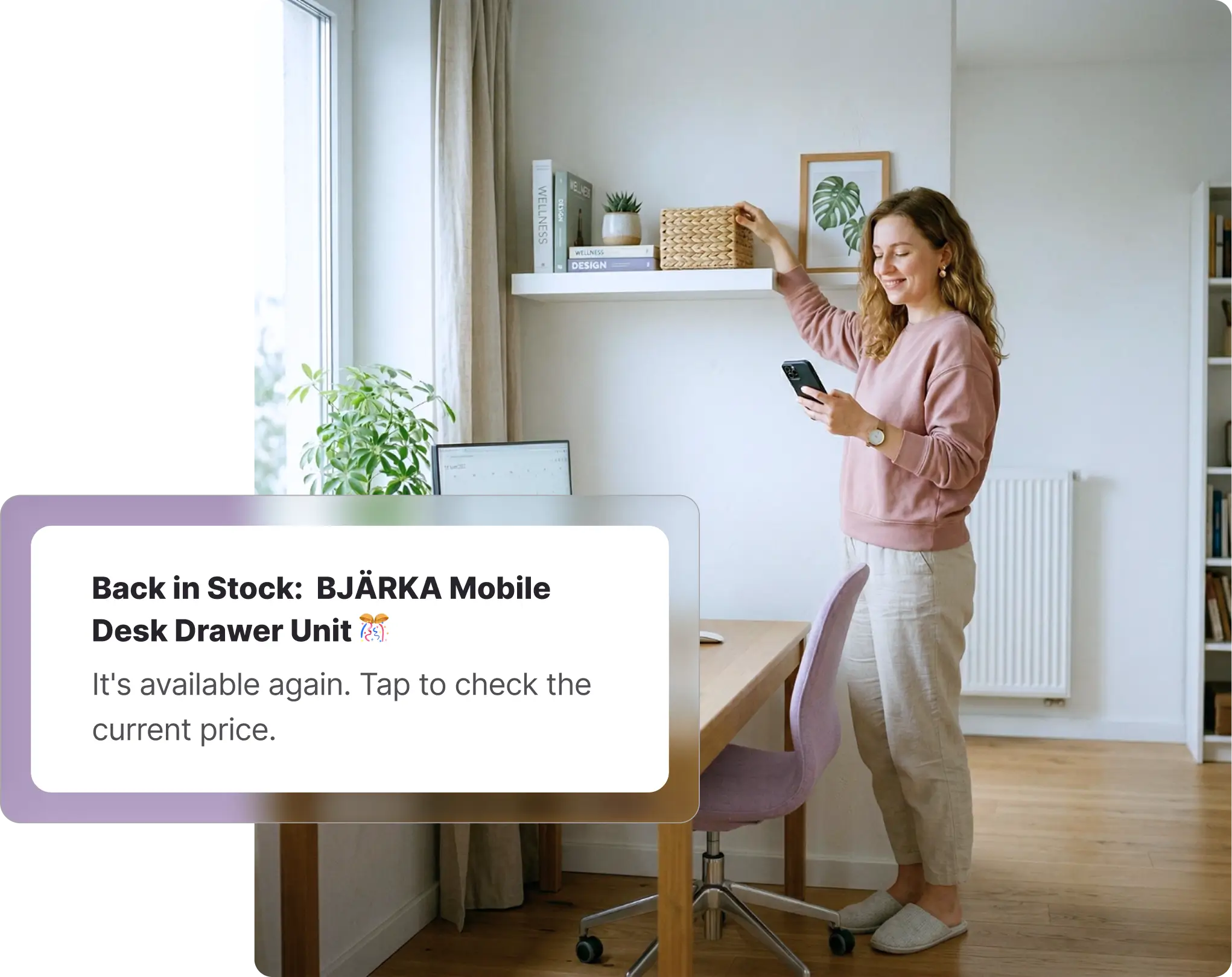 A smiling woman standing in a brightly lit home office looking at her smartphone while arranging items on a white floating wall shelf. Below her, a wooden desk with a purple office chair is visible. Overlaid on the image is a Whisprice digital notification displaying a back-in-stock alert for an IKEA product, specifically the "BJÄRKA Mobile Desk Drawer Unit," prompting the user to tap and check the current price.