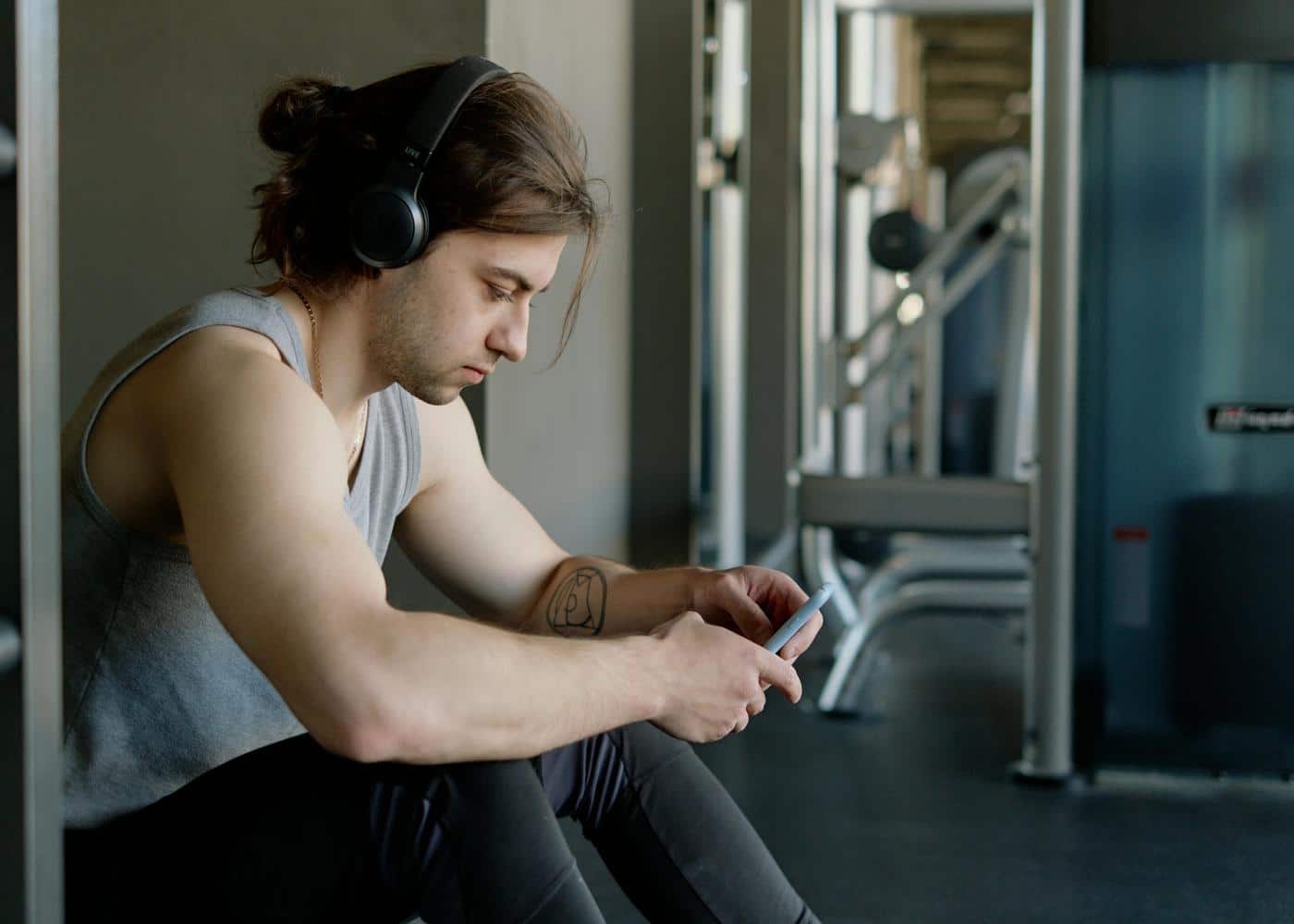 Man with heatphones on at gym sitting down looking at smartphone