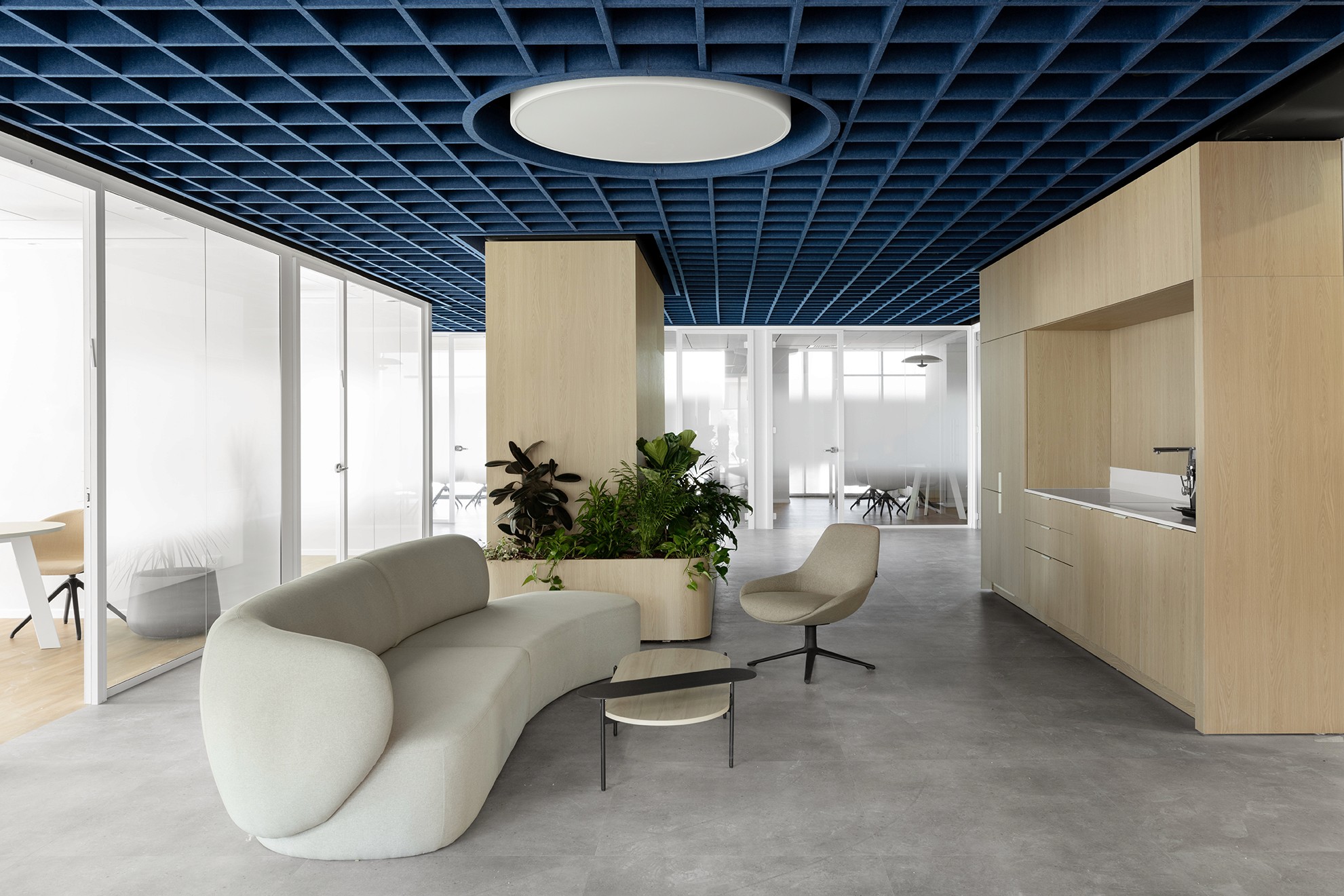 אזור המתנה במטה החברה: ספה פיסולית מעוגלת (Curved Sofa) בעיצוב נקי, הממוקמת מתחת לתקרת הגריד הכחולה המאפיינת את המשרדים.