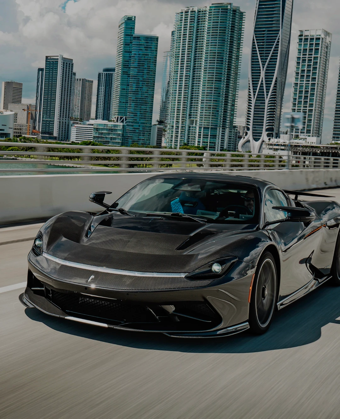 Black supercar driving across a Miami bridge with the city's skyline in the background, highlighting luxury and exotic car rentals available from Monarc VIP.