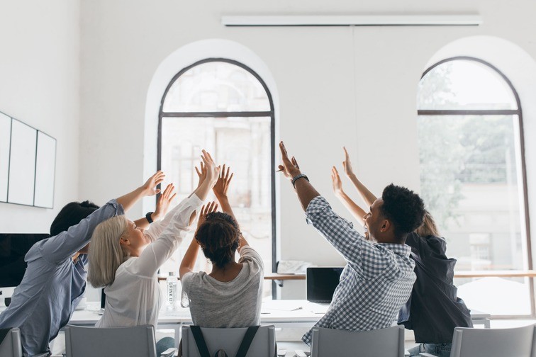 a team sitting on a desk holding their hands up