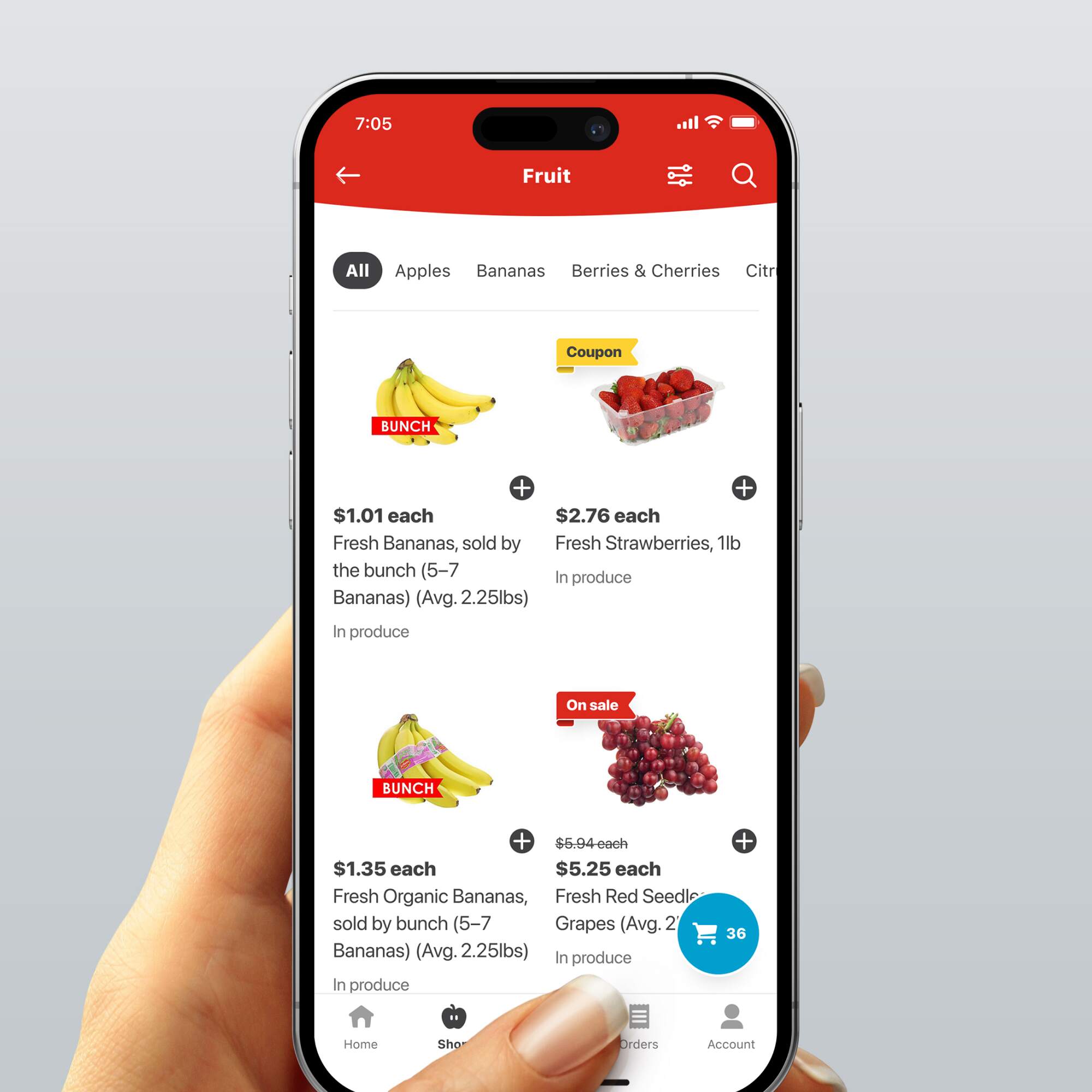 Hand holding a smartphone displaying the fruit category on the H-E-B app, showing prices and options for bananas, strawberries, and grapes.