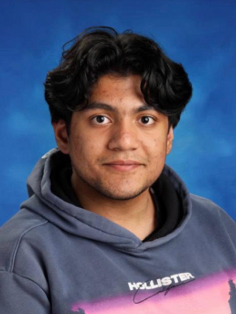 Smiling young man with curly hair, wearing a dark hoodie, against a softly lit background.