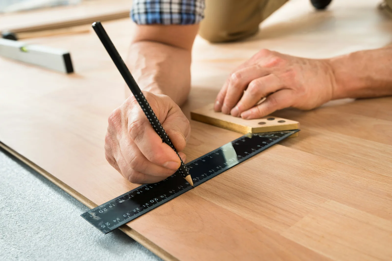 Craftsman marking laminate plank with pencil and metal ruler