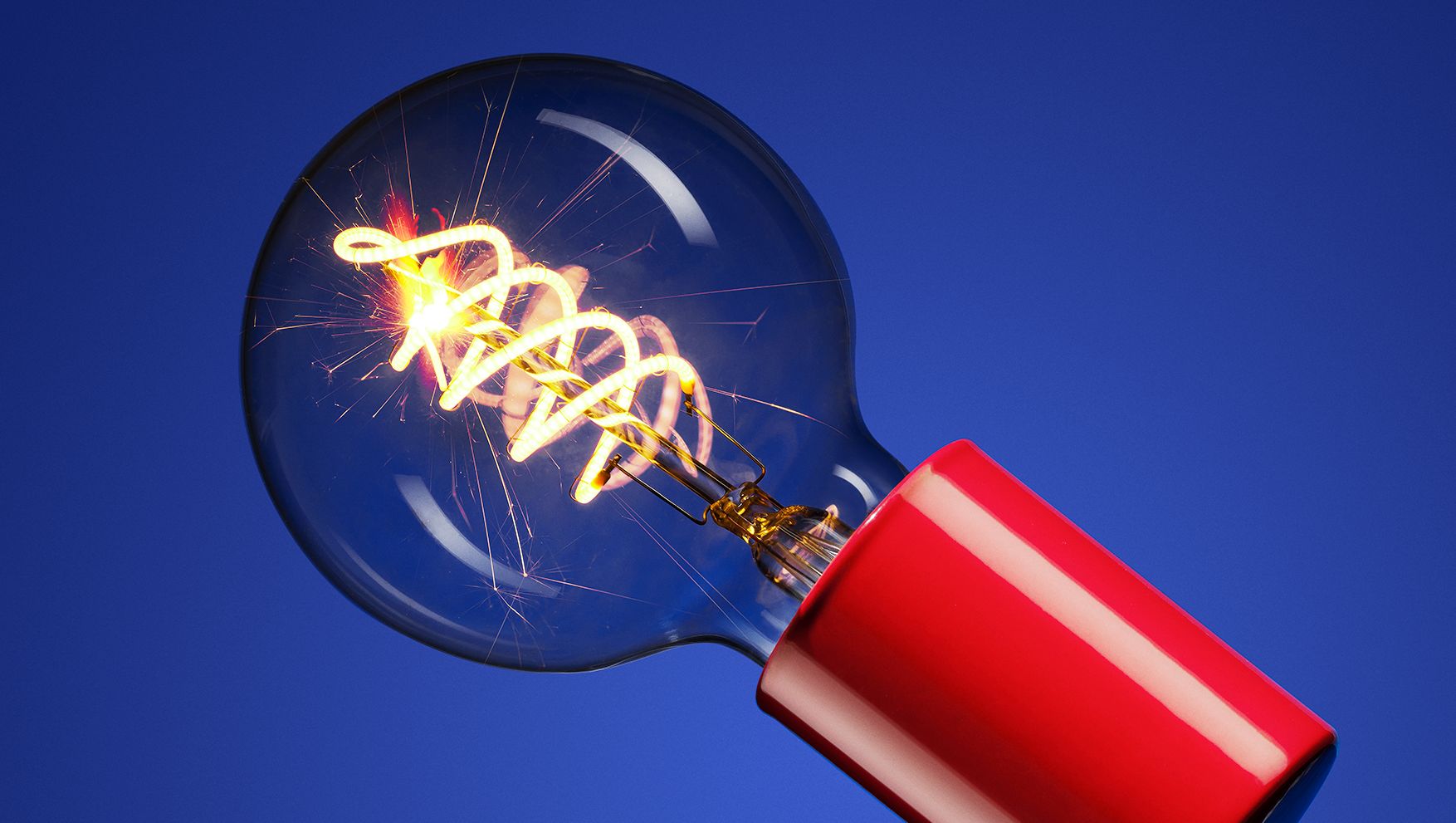 A round, clear lightbulb with sparkling elements inside, affixed to a glossy red socket, set against a blue background.