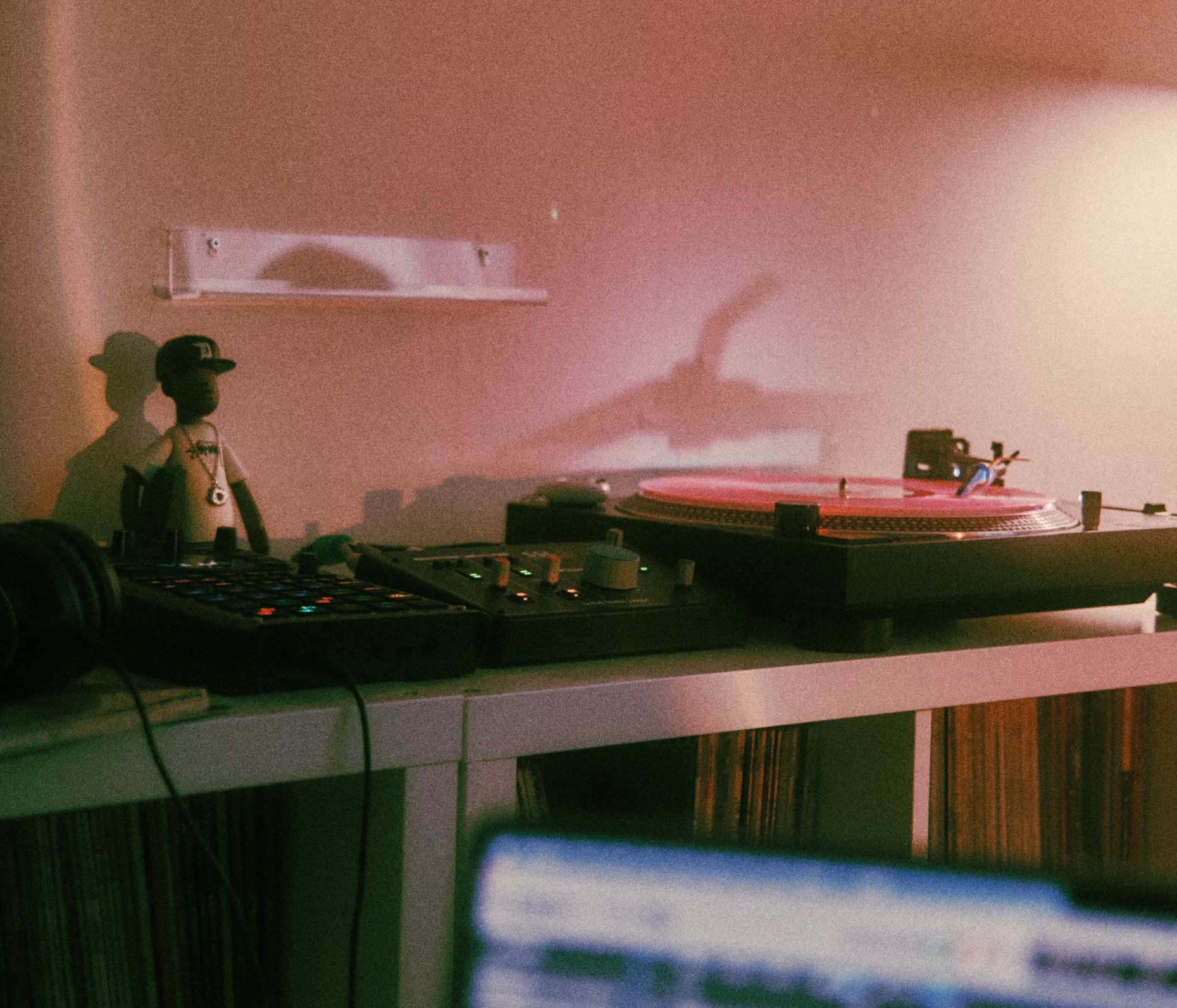 Minimal desk setup with a turntable, small figurines, and soft ambient lighting against a warm-toned wall.