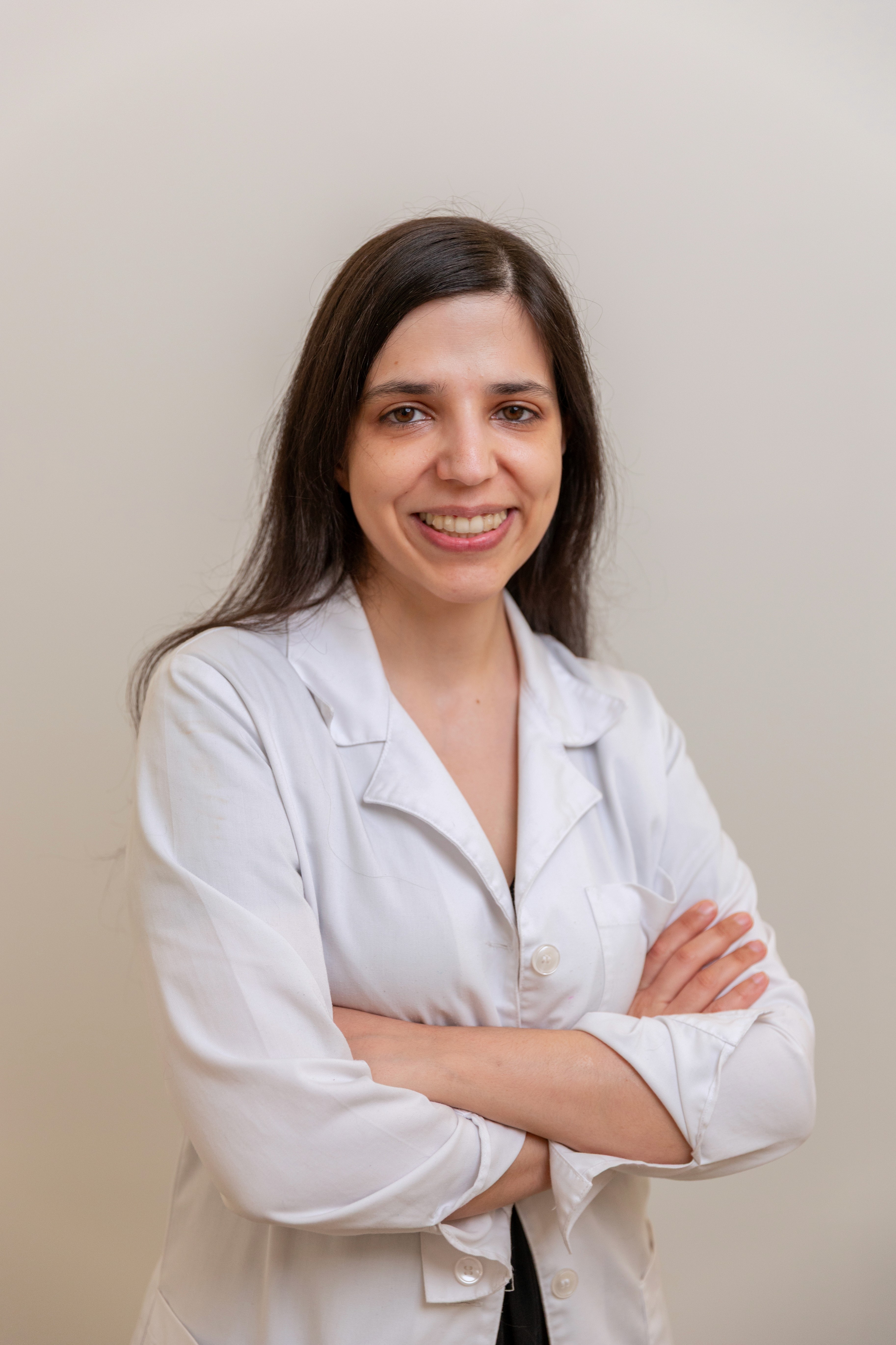 Smiling female doctor wearing a white coat, standing with arms crossed in a clinic setting.