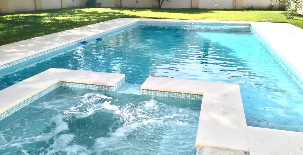 Amplia pileta de jardín revestida en venecitas celestes claras, destacando un sector de jacuzzi con sistema de hidromasaje en pleno funcionamiento.