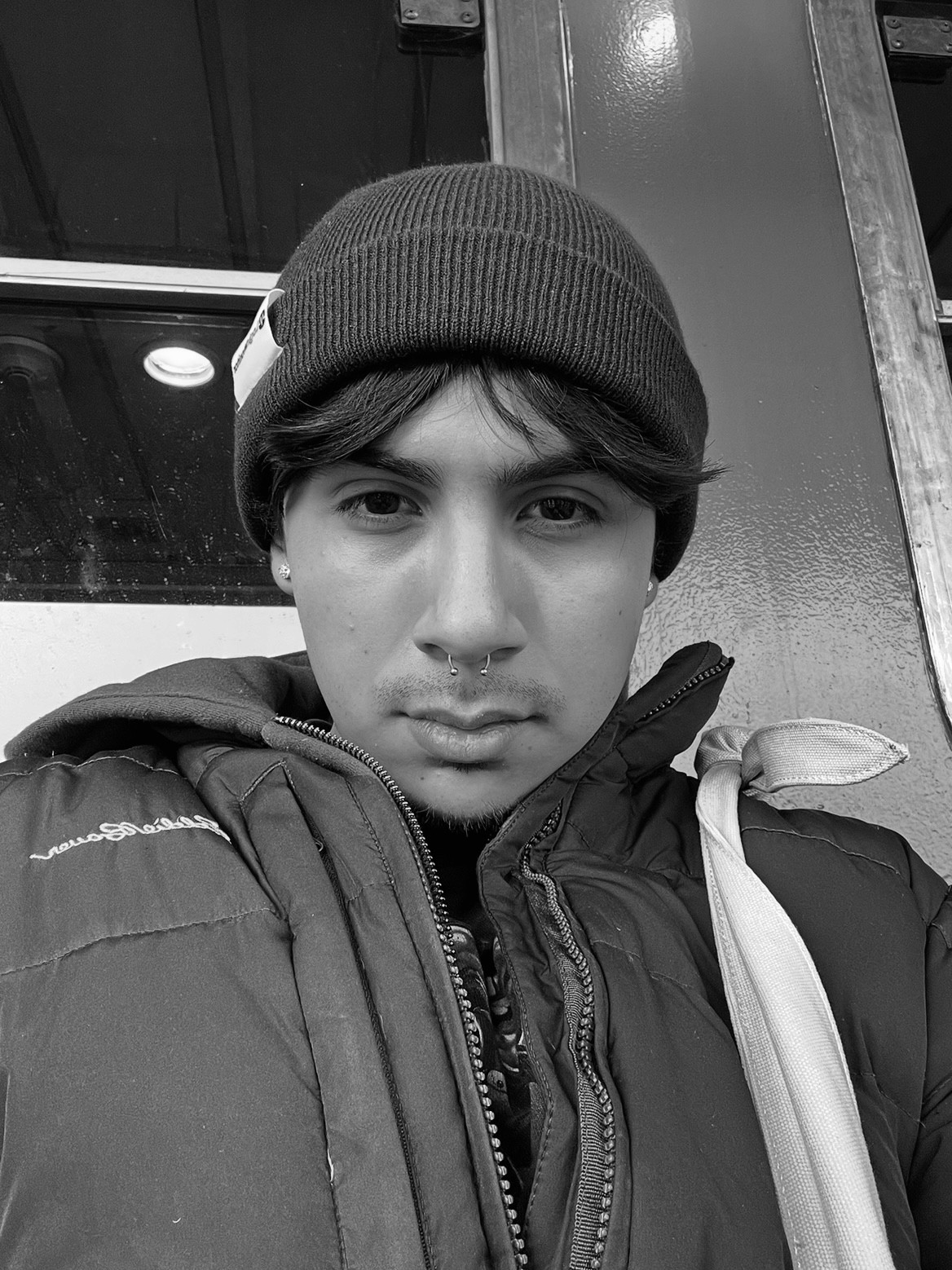 A thoughtful young person with dark hair gazes to the side, captured in soft black and white lighting.