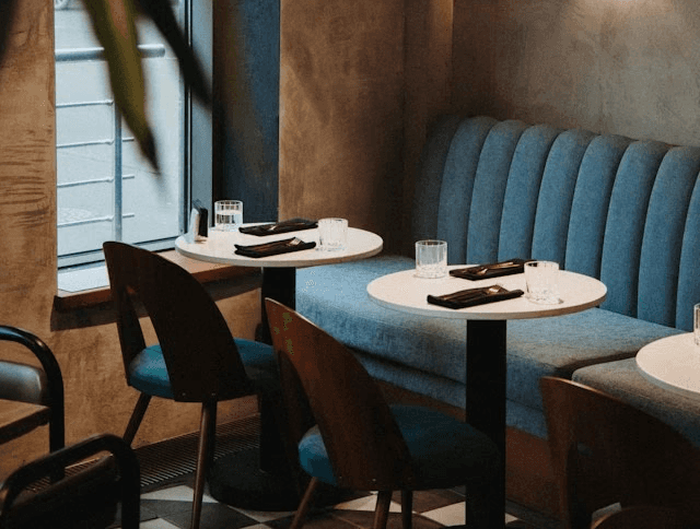 Gemütliches Café mit Holzstühlen, runden Tischen und blauer Sitzbank