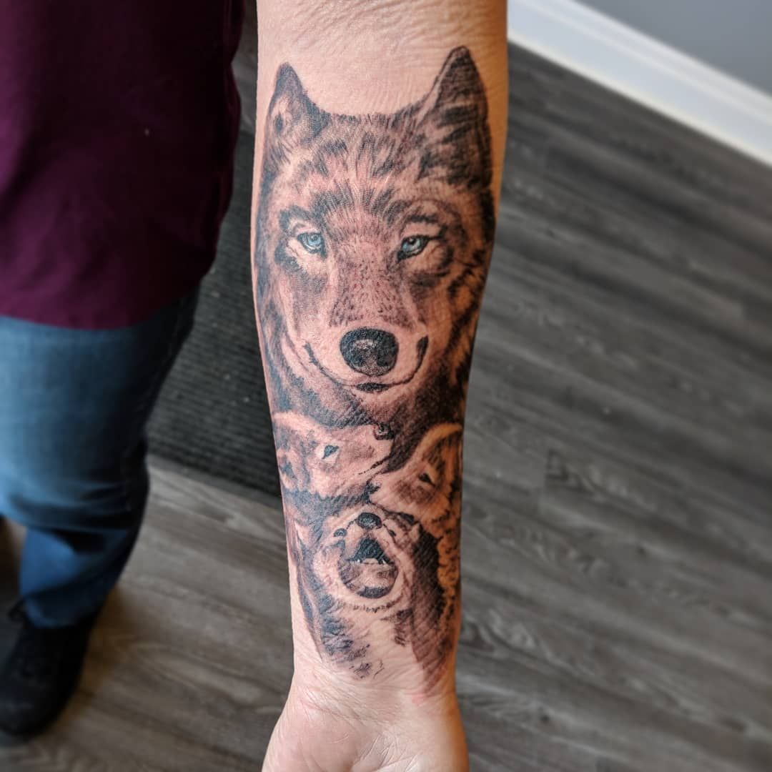 Black-and-grey wolf and forest sleeve tattoo on an arm