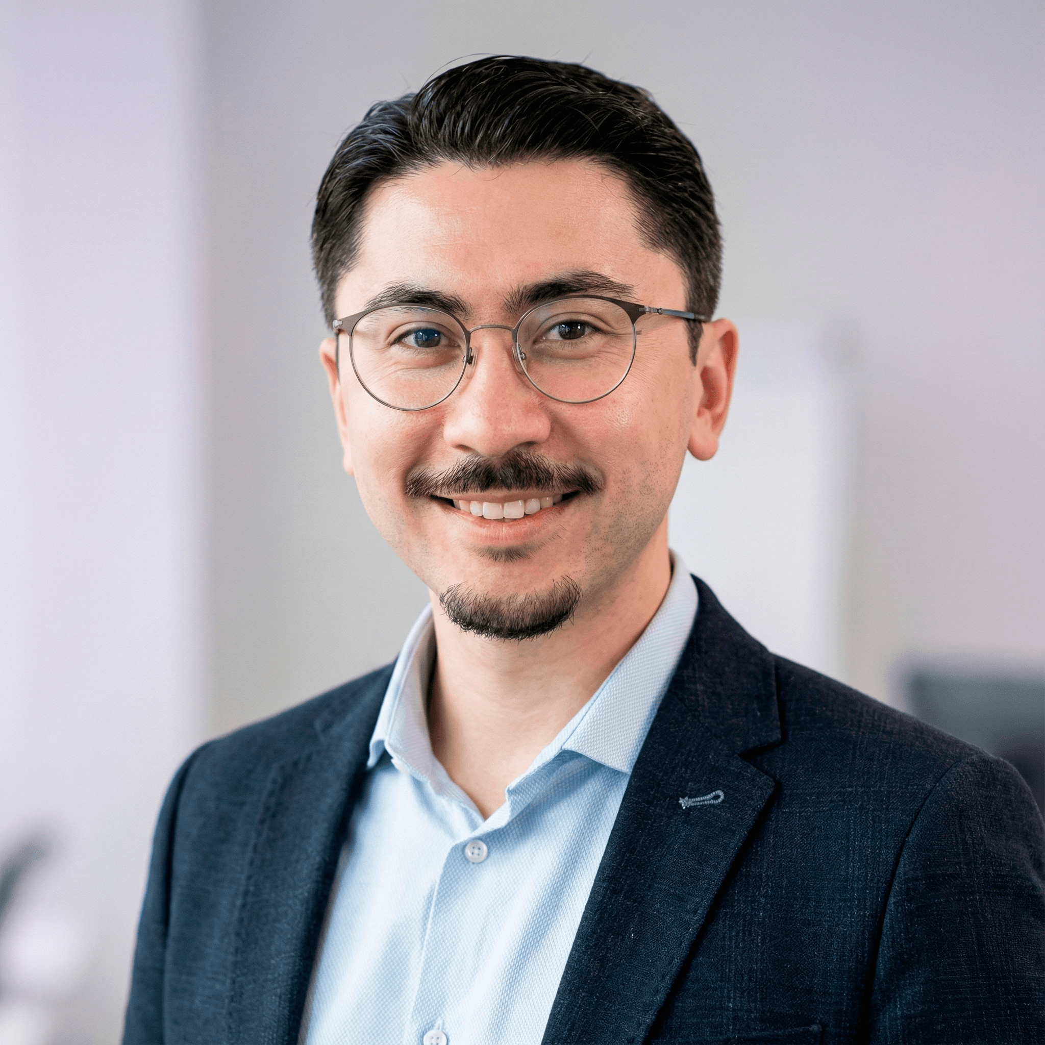 Young man with wavy hair wears a dark overcoat, rust-colored sweater, white shirt, and patterned tie, exuding a poised and sophisticated demeanor.