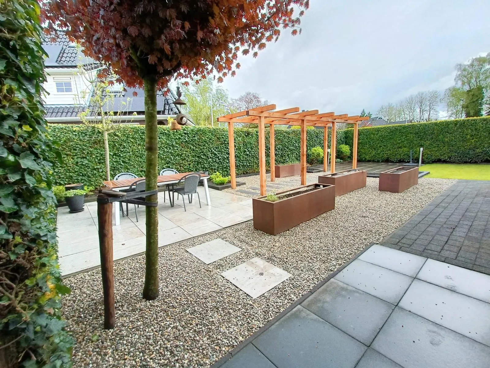 Tuinaanleg in moderne achtertuin met grind, plantenbakken van cortenstaal, houten pergola en terras in Gorredijk