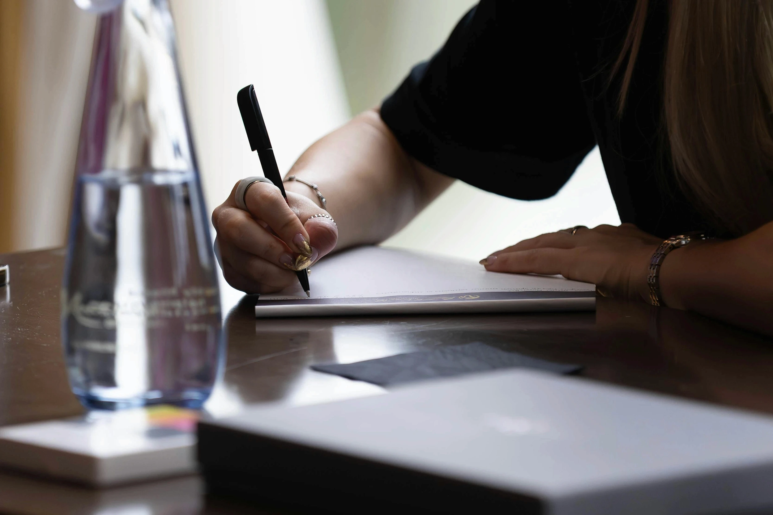 Business woman writing document on wooden table with glass bottle of water.
