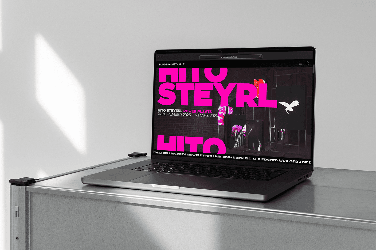 A laptop on a surface displaying vibrant pink text against a dark background. Sunlight casts shadows nearby.