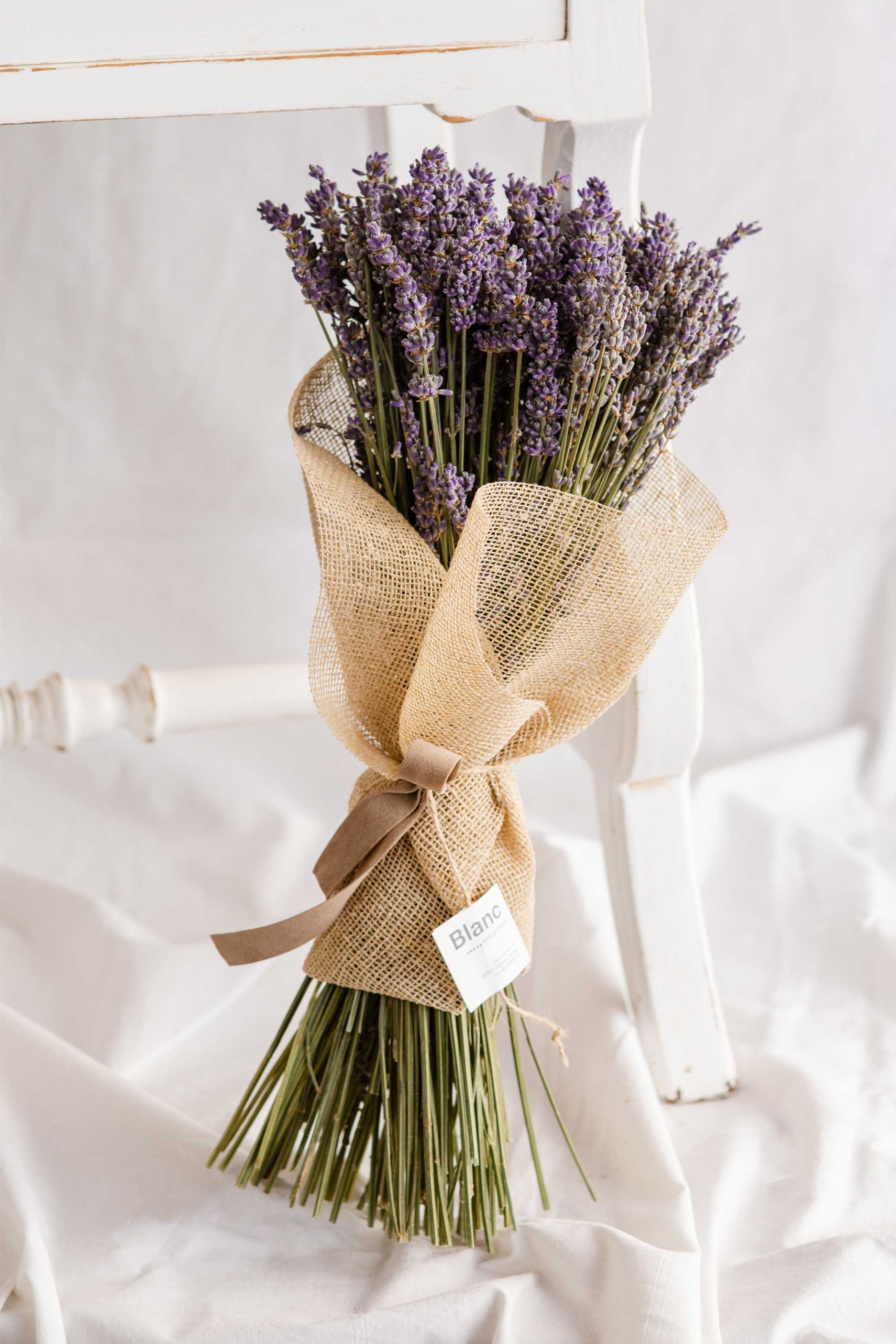 Ram de lavanda seca embolcallat amb tela de jute i llaç de vellut, recolzat sobre una cadira blanca de fusta.