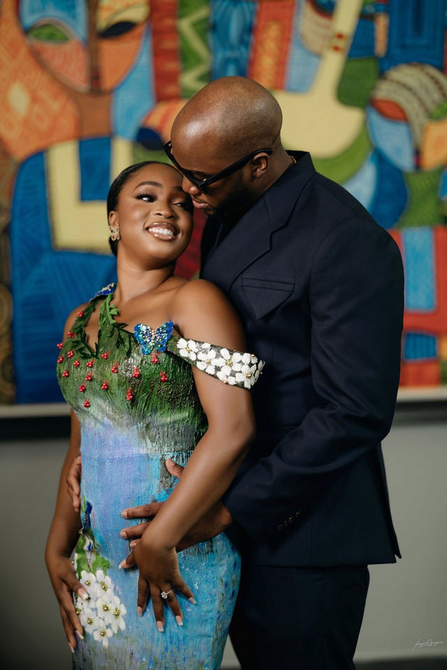A smiling woman with her arms crossed, standing against a dark green background. She has long, dark hair.