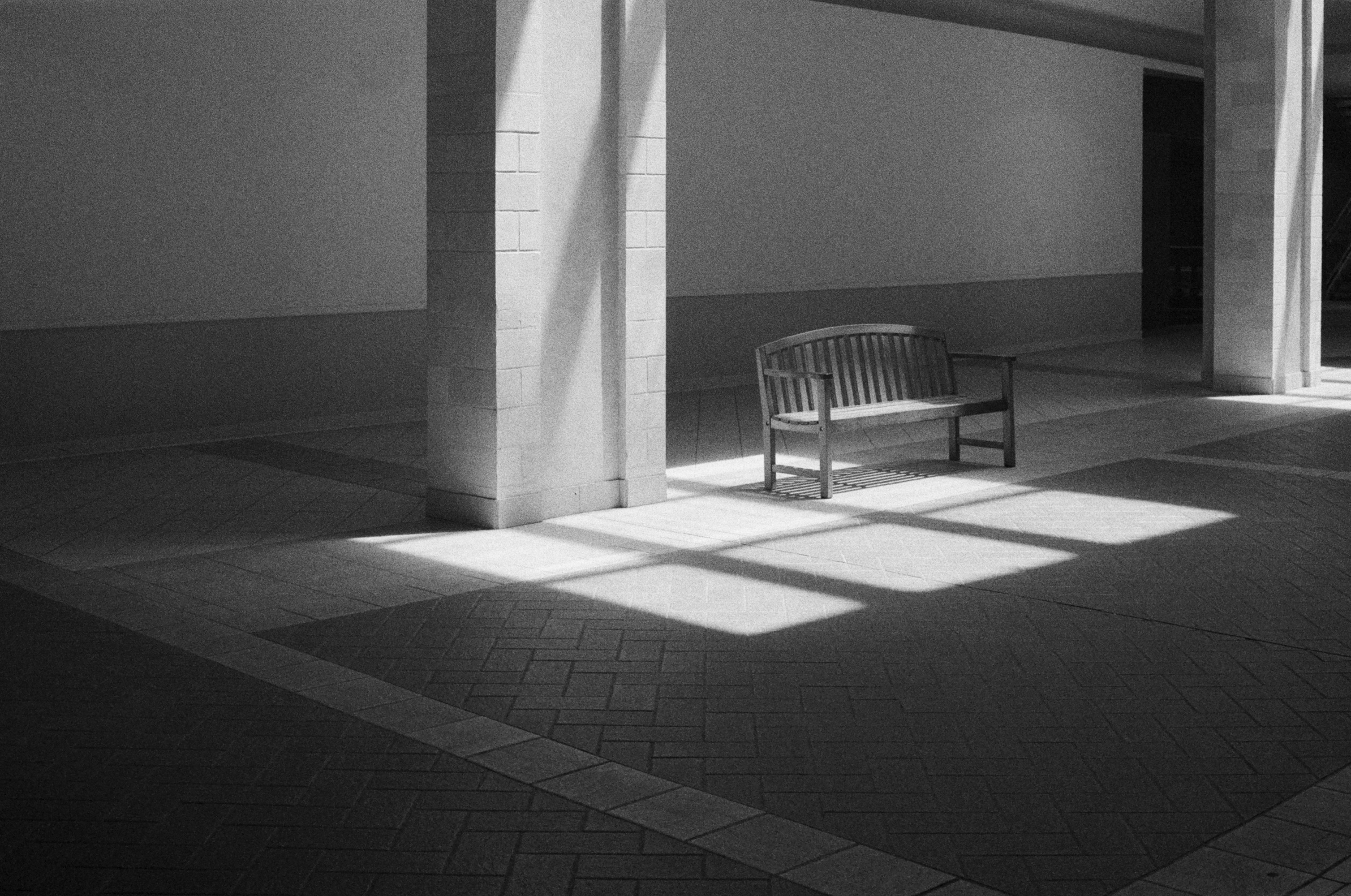 Wooden bench in sunlight with geometric shadows on floor.