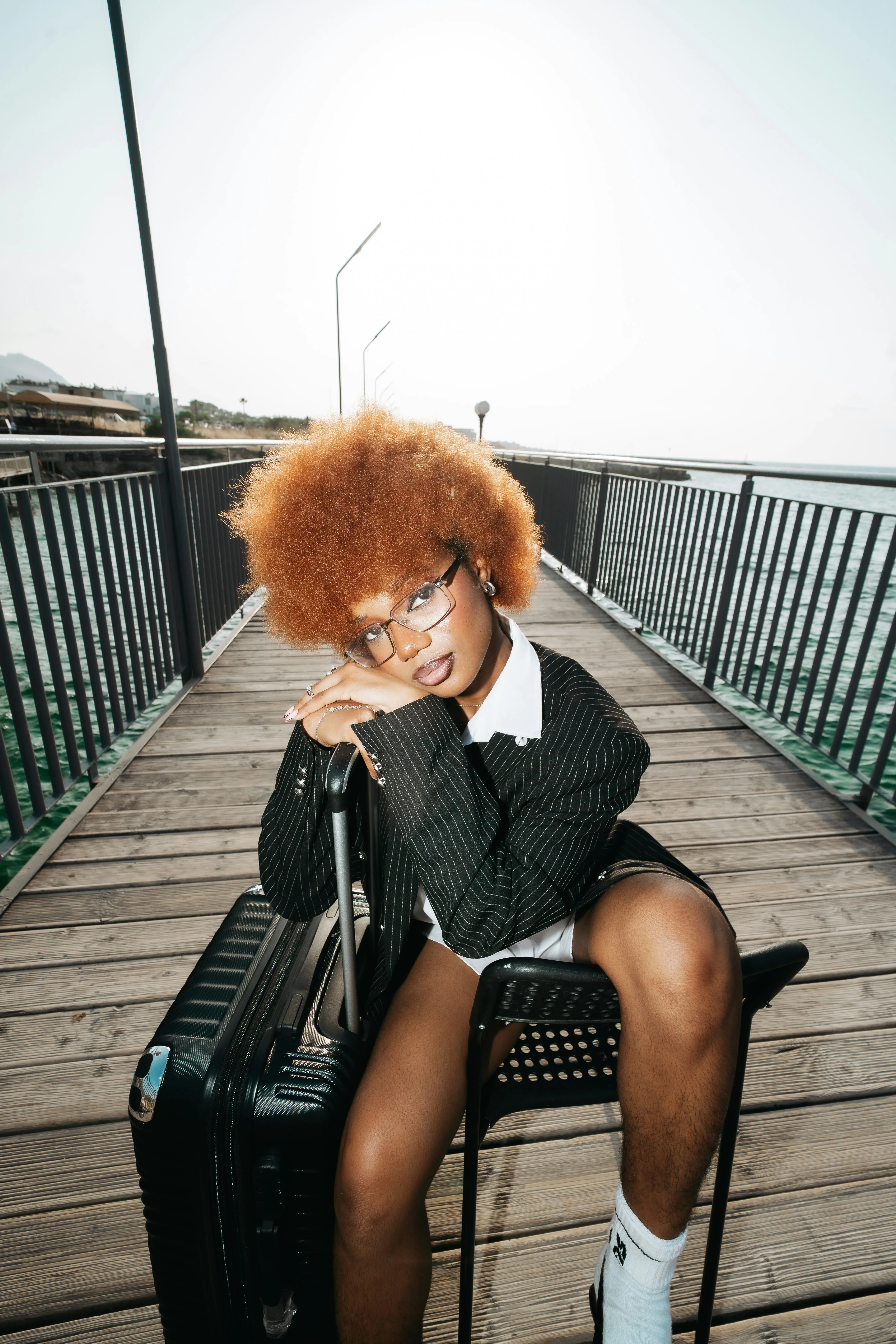 A person with an afro hairstyle wearing a pinstripe blazer on a wooden pier