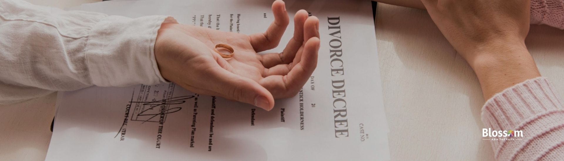 Two hands holding wedding rings over a divorce decree document