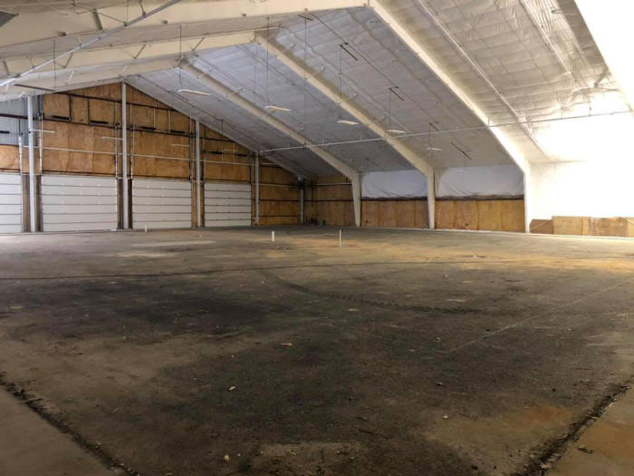 A spacious indoor area with high ceilings, wooden walls, and an empty concrete floor.