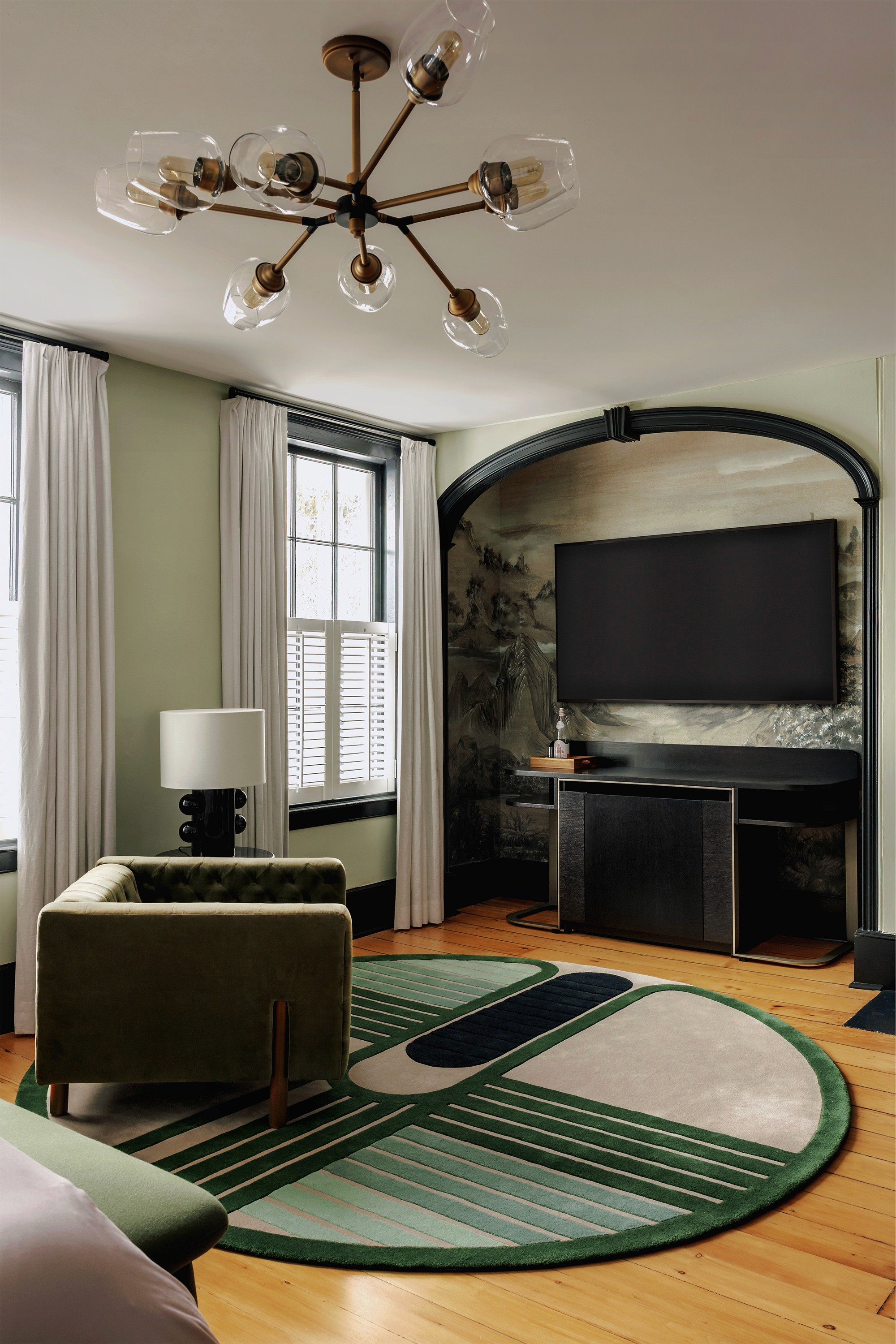 Hattan House principal bedroom lounge area, Kelly Wearstler Tiglia table lamp beside sputnik chandelier and green velvet armchair against sage walls