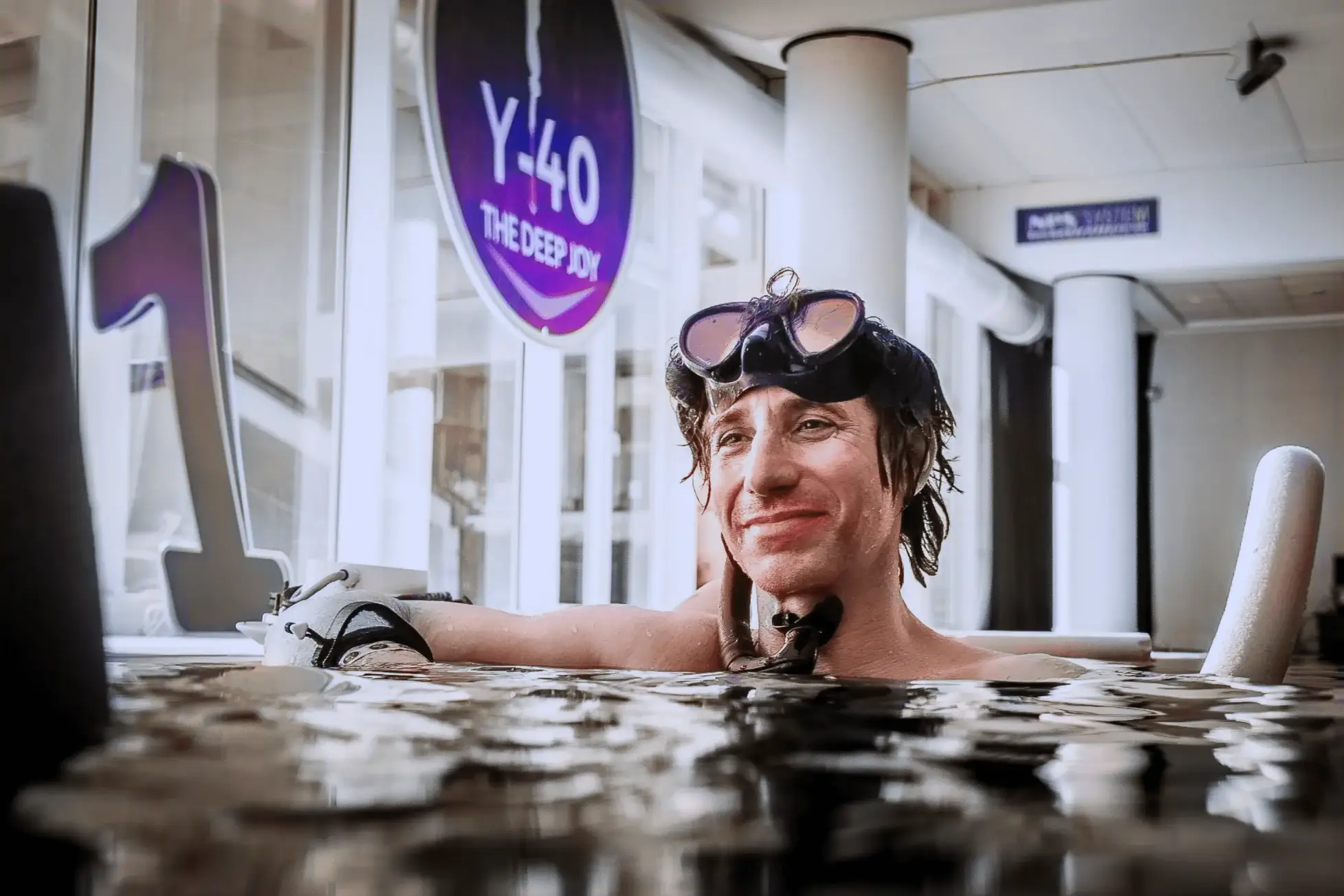 Mathias dans une piscine, portant des lunettes de natation, regarde la caméra avec un léger sourire.